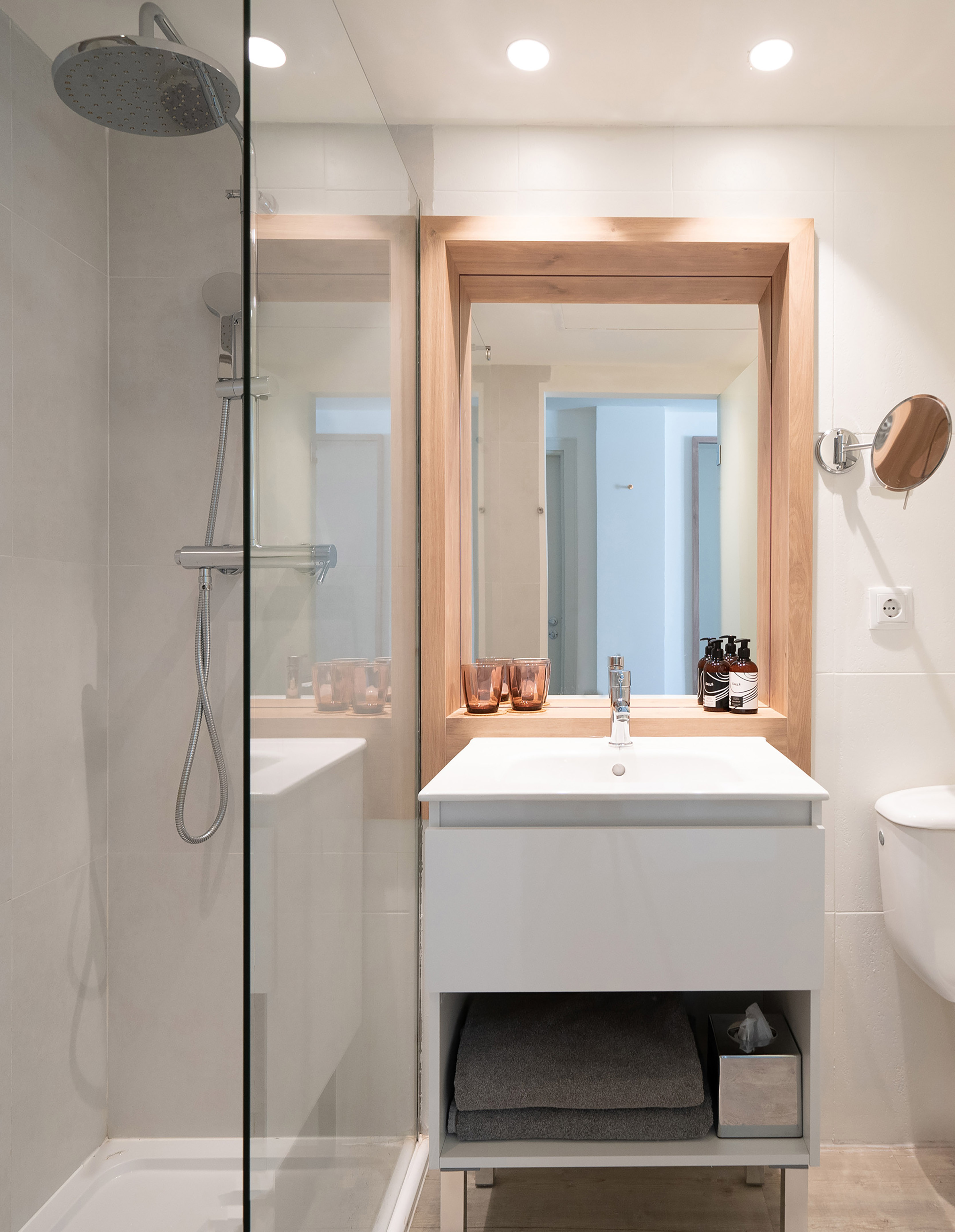 Modern bathroom with walk-in shower, white vanity, and wooden mirror frame.