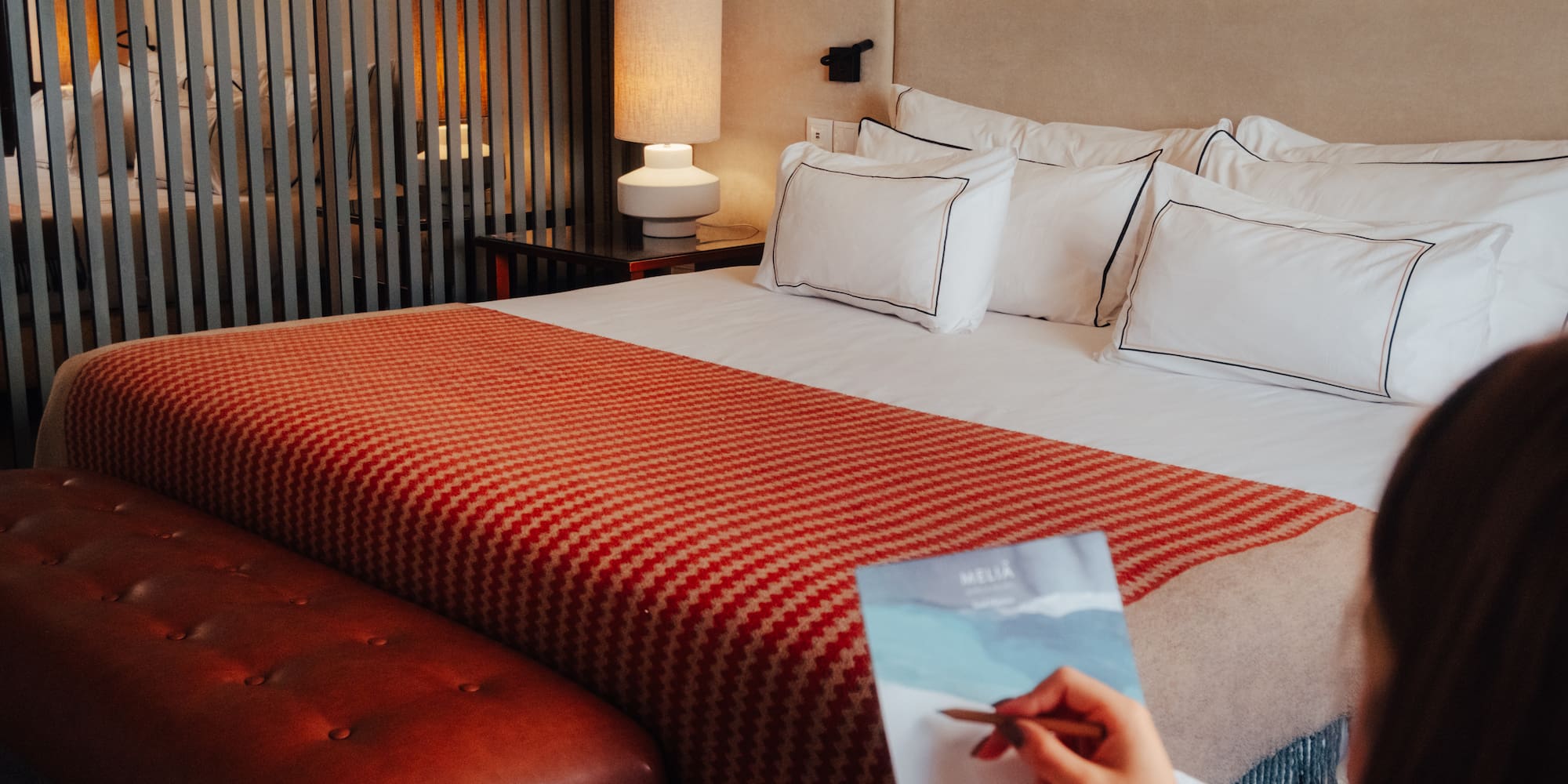 Meliá hotel room with cozy bed, orange throw, leather bench, and guest writing.