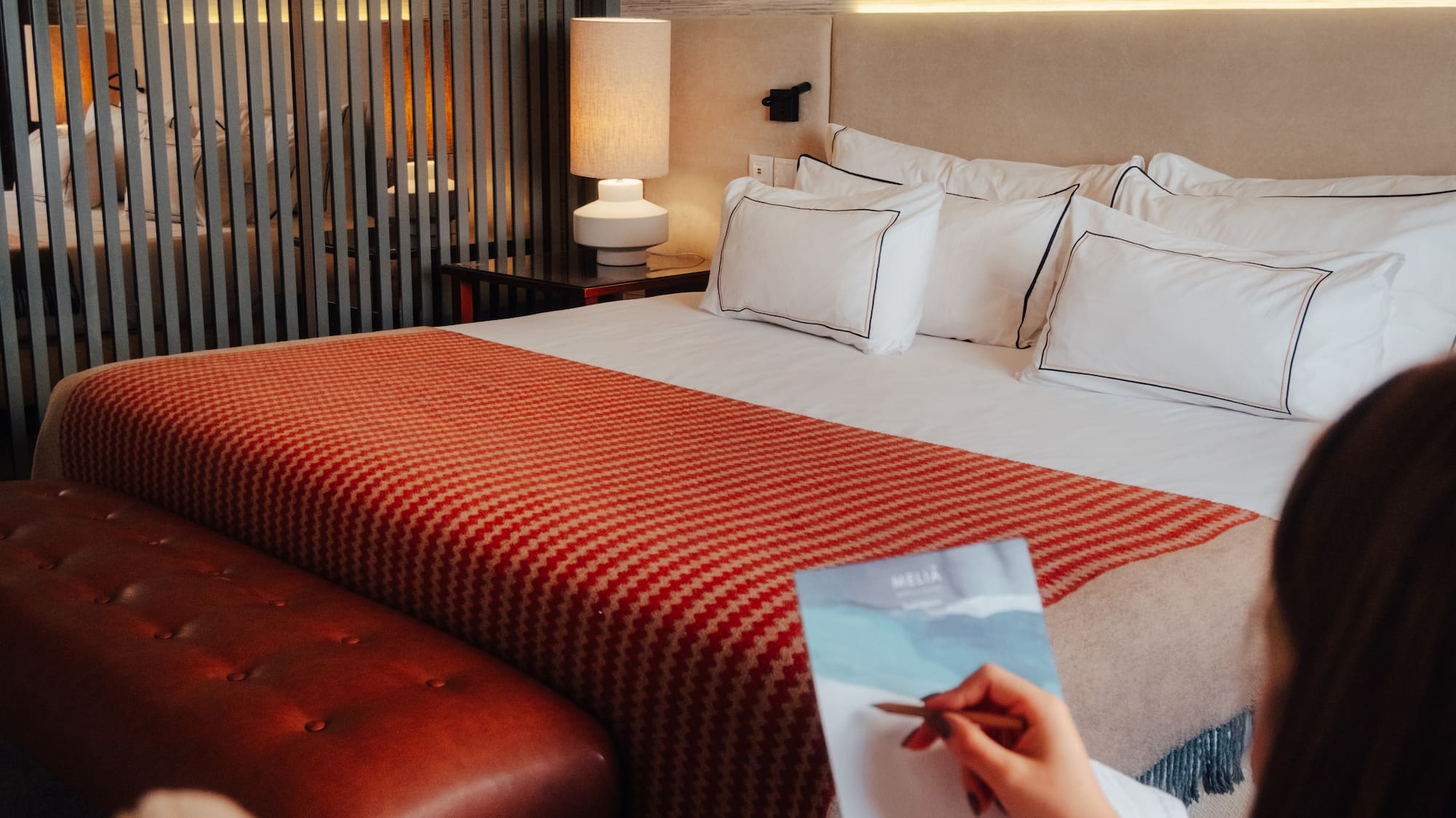Meliá hotel room with cozy bed, orange throw, leather bench, and guest writing.