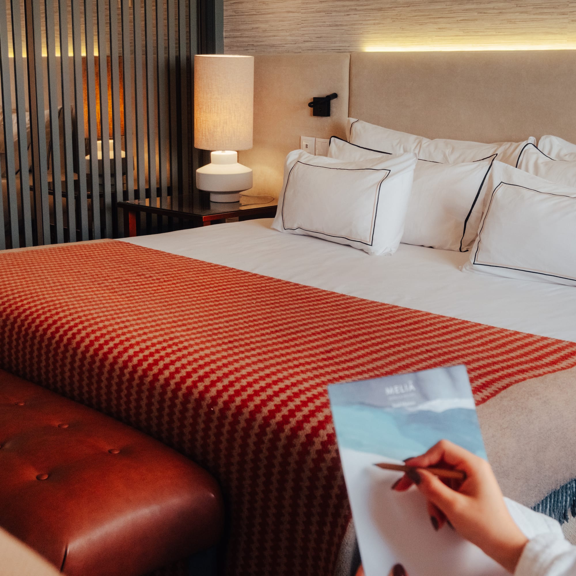 Meliá hotel room with cozy bed, orange throw, leather bench, and guest writing.
