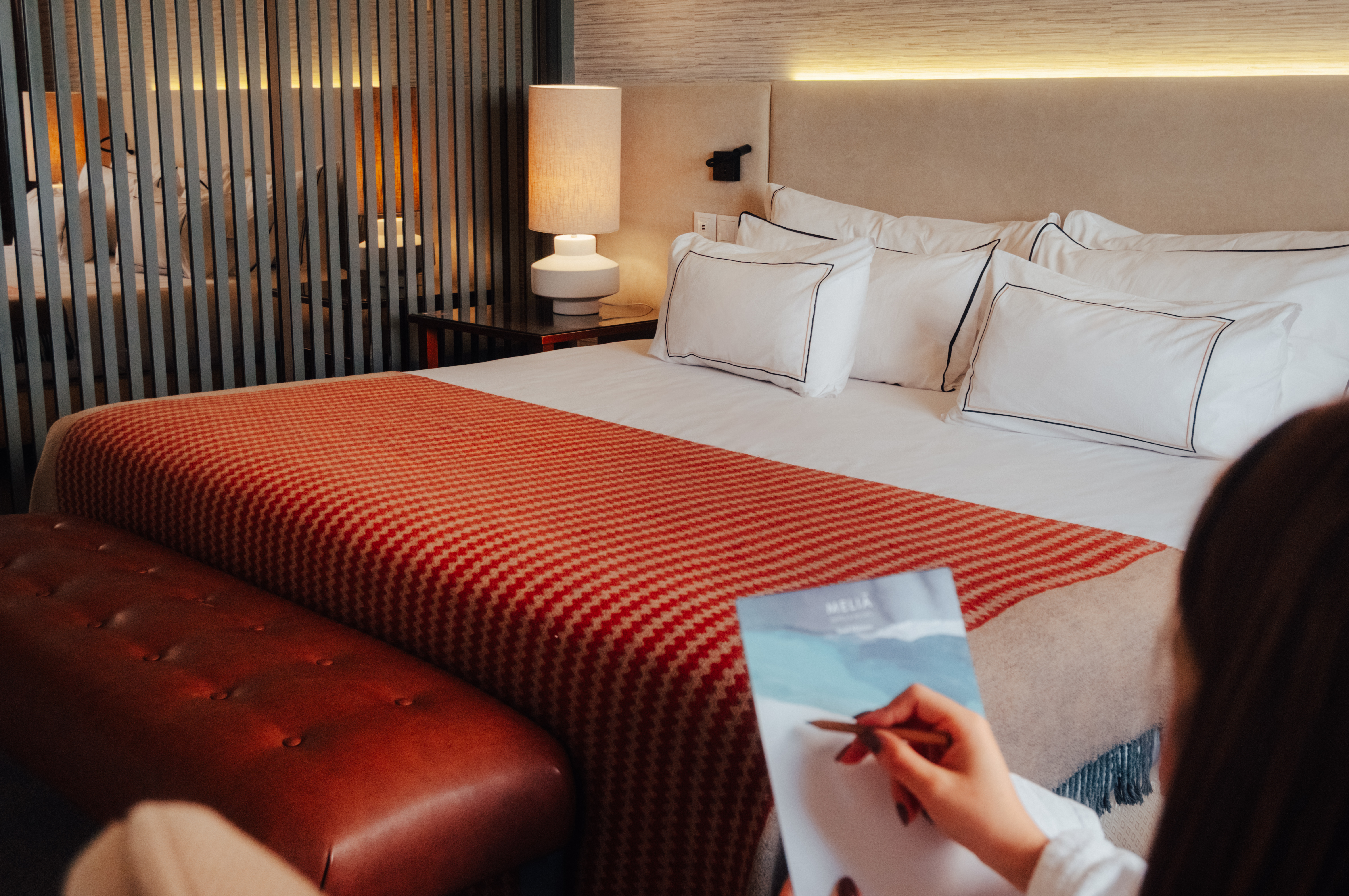 Meliá hotel room with cozy bed, orange throw, leather bench, and guest writing.