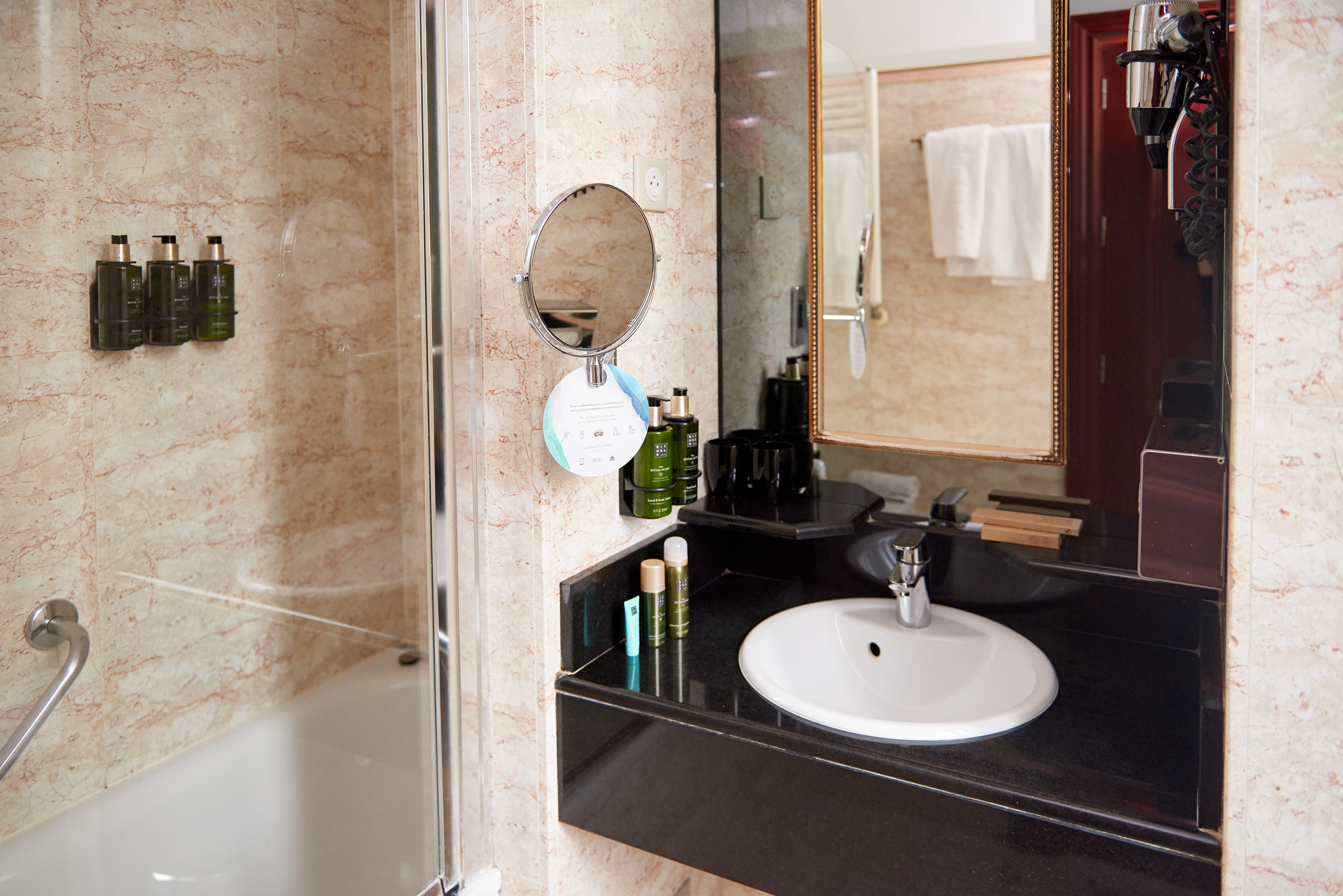 Hotel bathroom vanity with sink, magnifying mirror, bathtub, and eco-friendly toiletries.