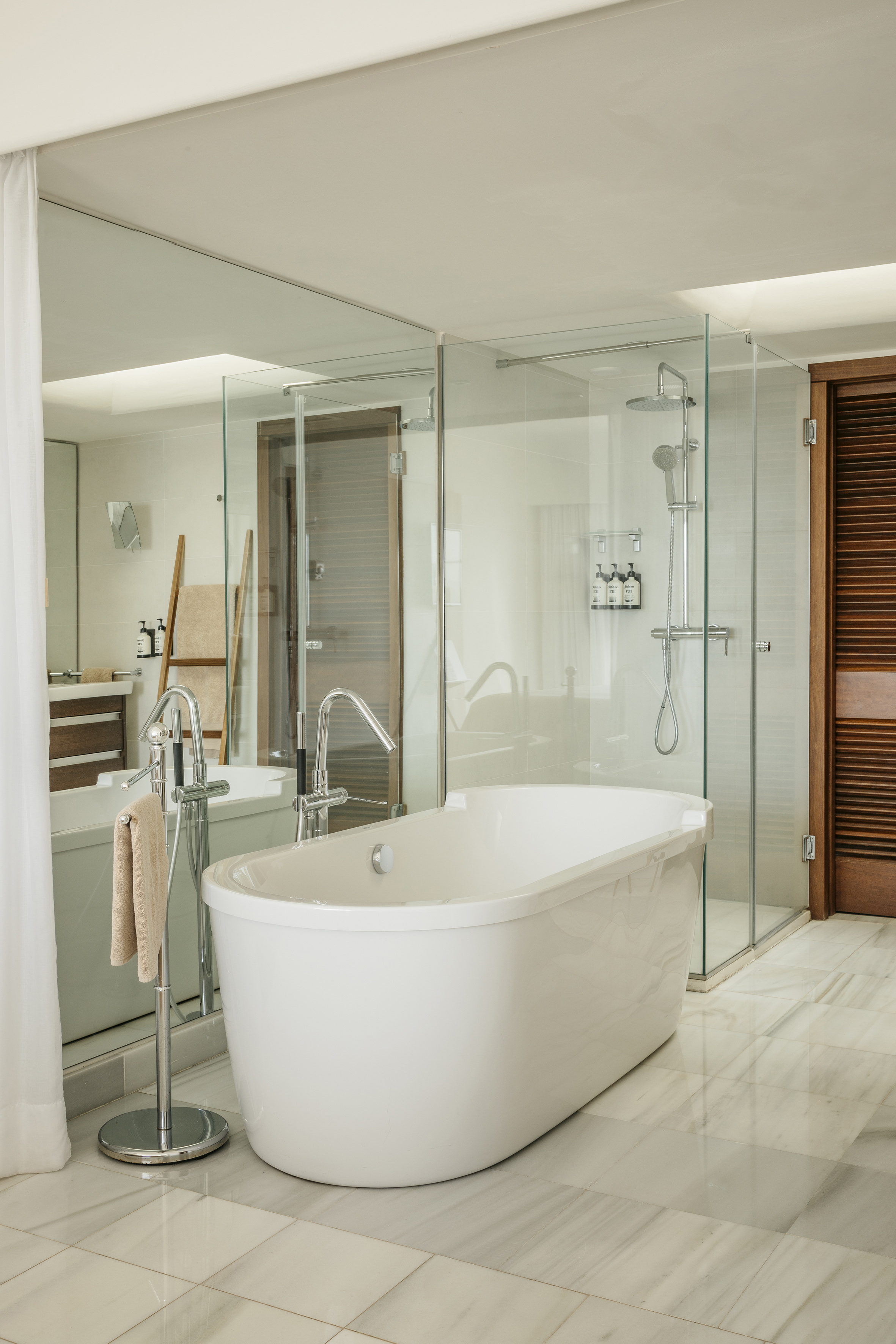Modern bathroom with freestanding tub, glass shower, and marble floor.