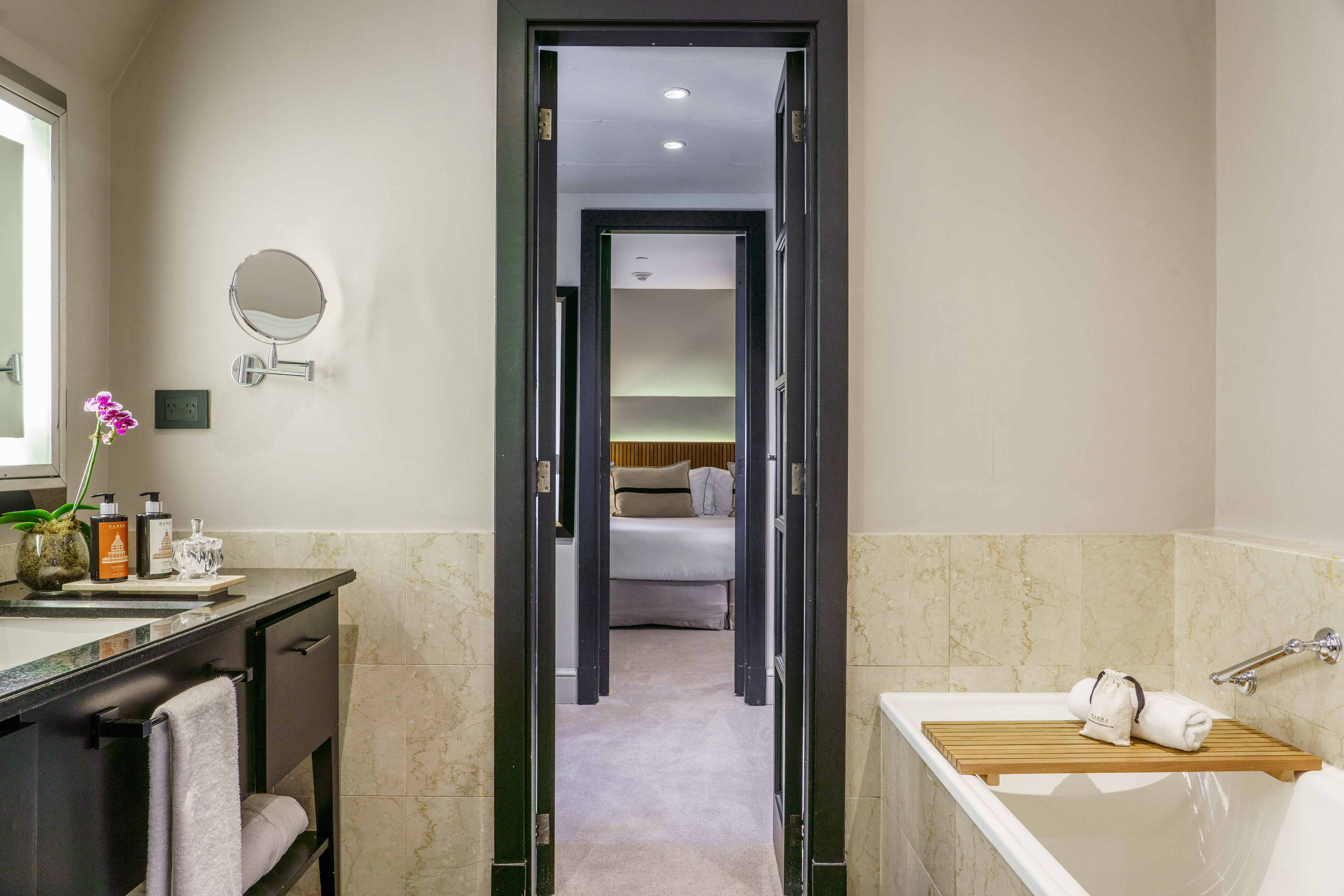 Luxury bathroom with vanity, tub, and doorway to stylish hotel bedroom.