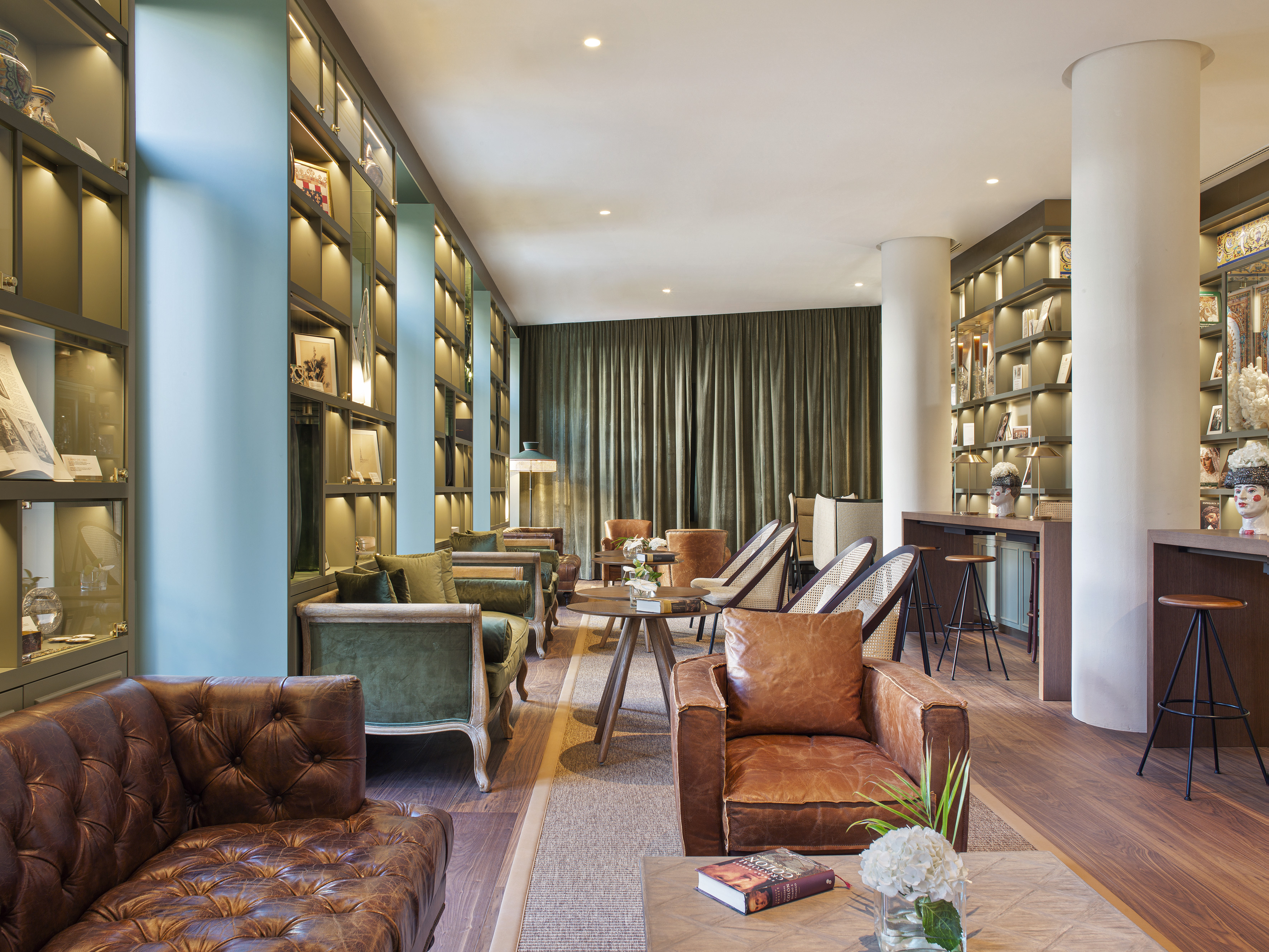 Hotel lounge with brown leather and green velvet seating, library shelves, bar.