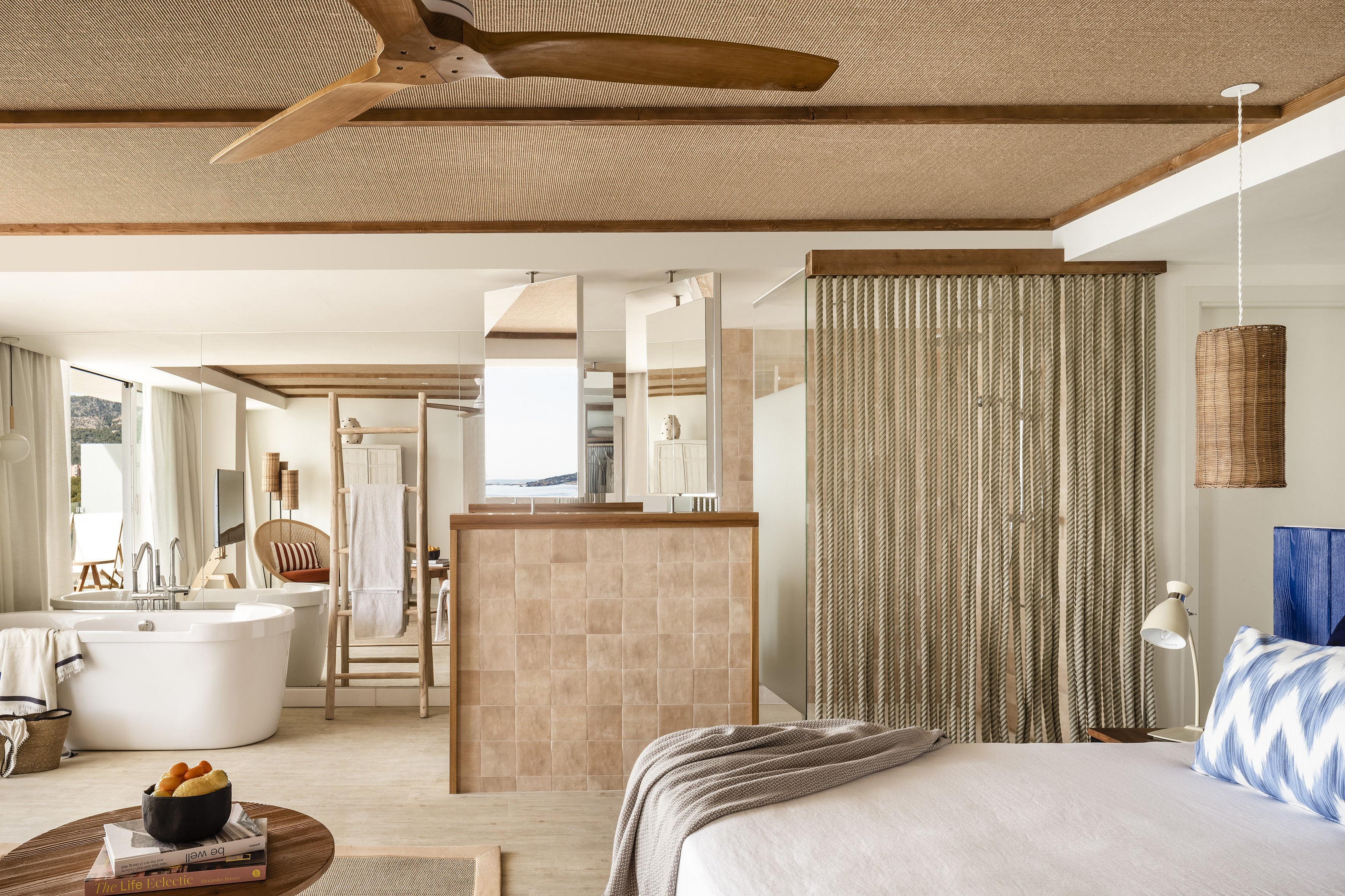 Luxury hotel bedroom with bathtub, wood fan, rattan ceiling, and sea view.