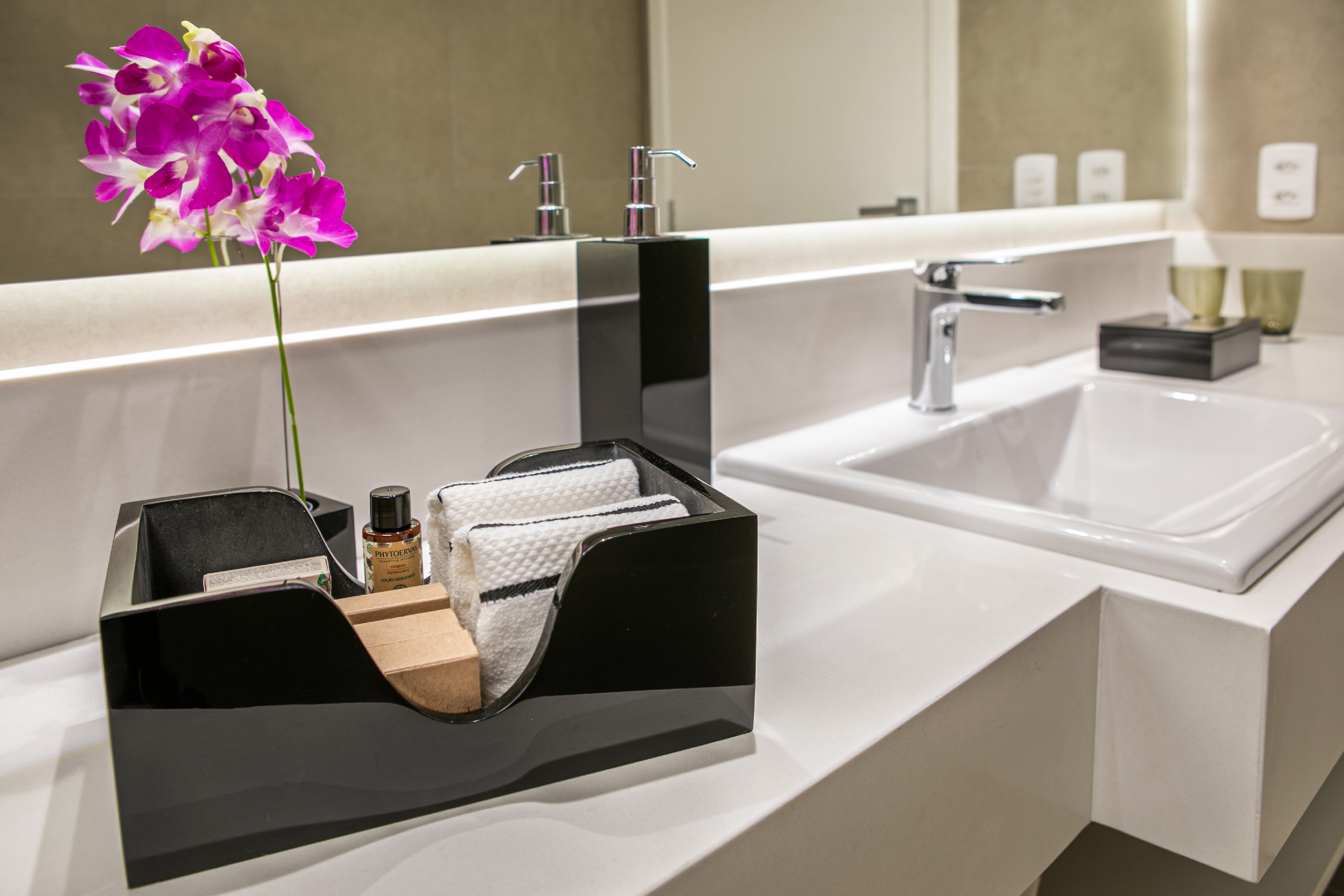 Modern bathroom vanity, white sink, purple orchids, and guest toiletries.