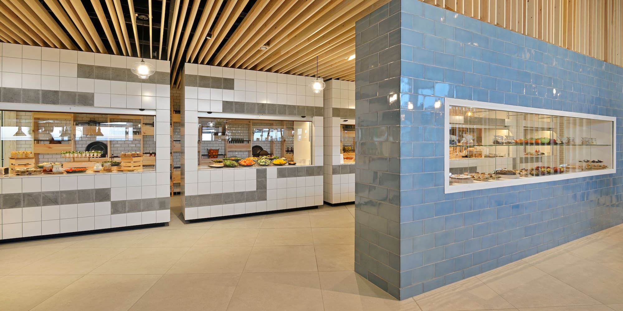 Modern cafeteria buffet with fresh food, tiled counters, and blue dessert display.