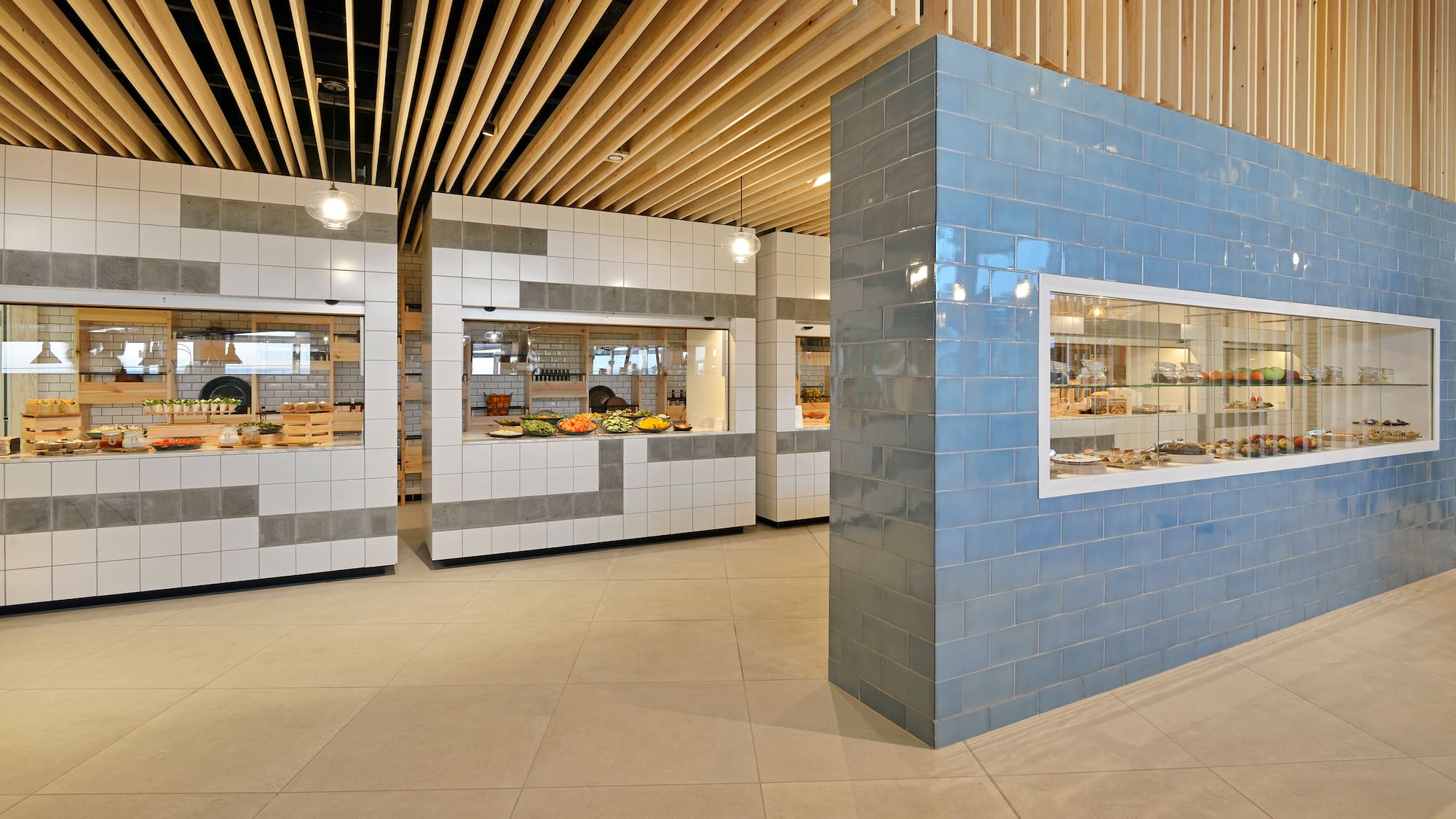 Modern cafeteria buffet with fresh food, tiled counters, and blue dessert display.