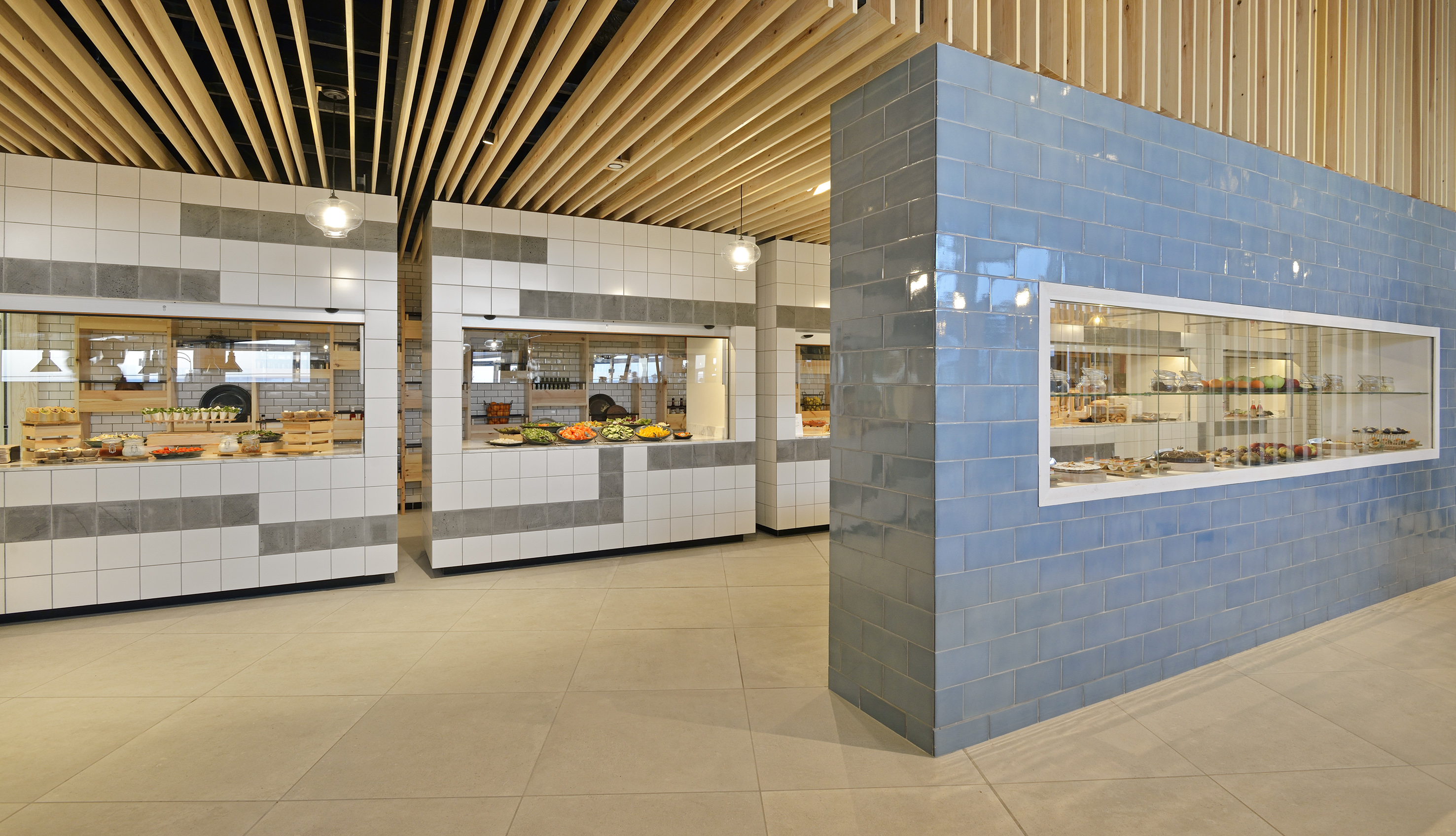 Modern cafeteria buffet with fresh food, tiled counters, and blue dessert display.