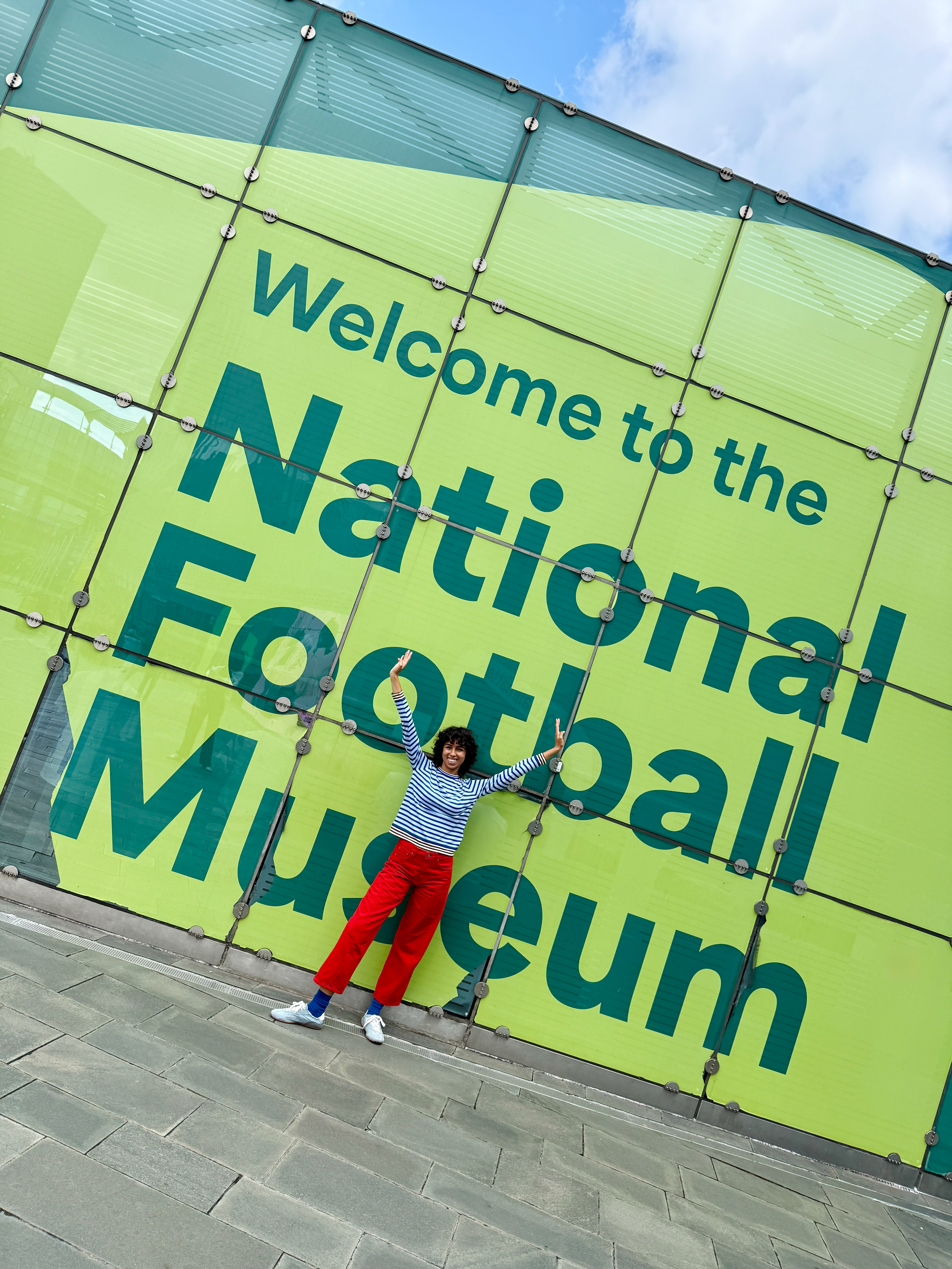 Woman posing in front of the National Football Museum welcome sign.