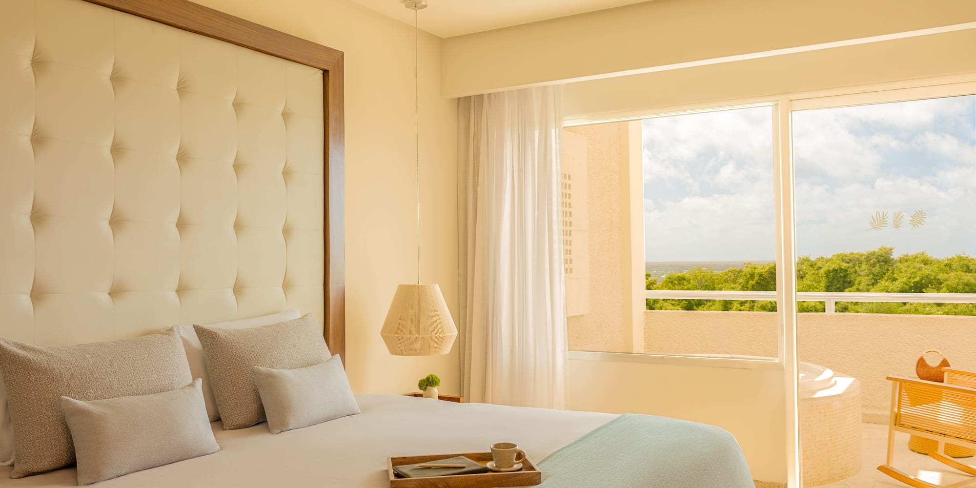 Hotel bedroom with balcony ocean view, tufted bed, and outdoor hot tub.