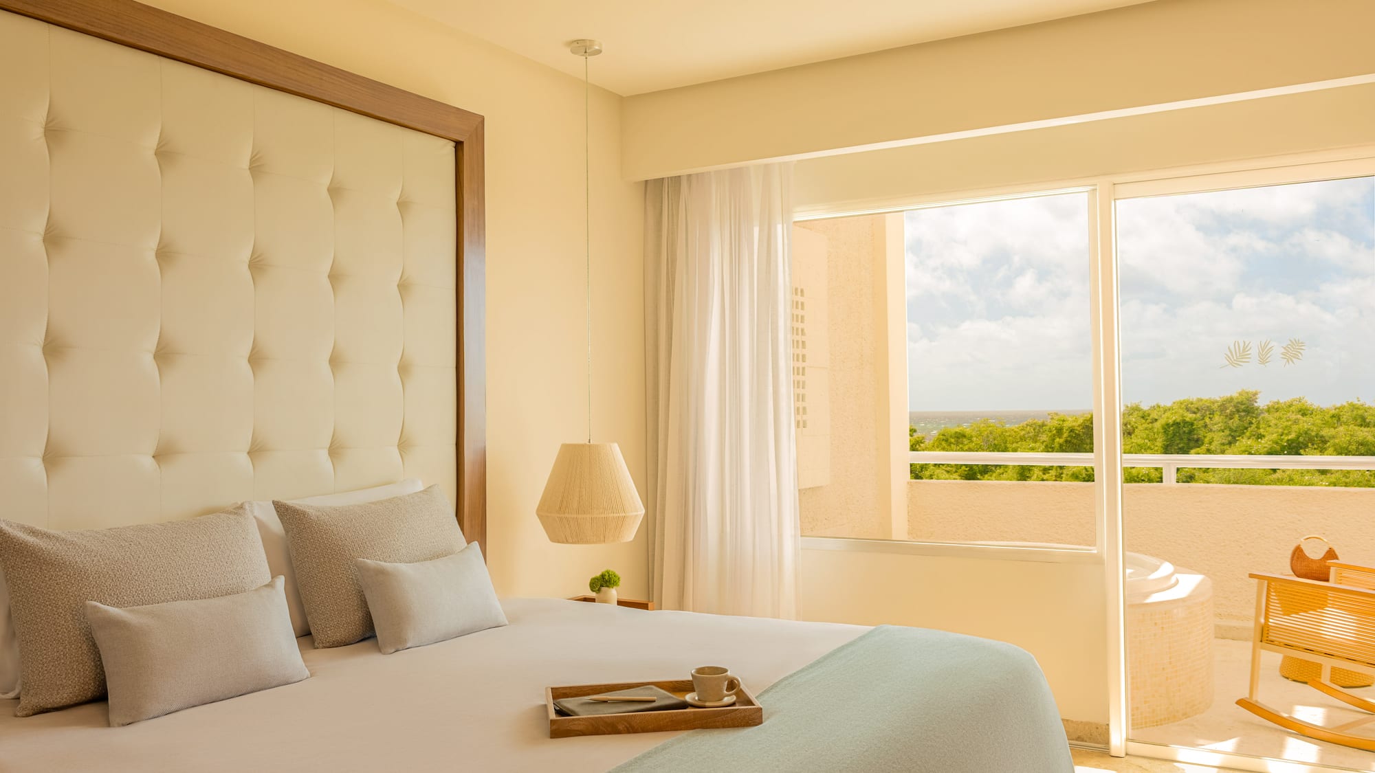 Hotel bedroom with balcony ocean view, tufted bed, and outdoor hot tub.