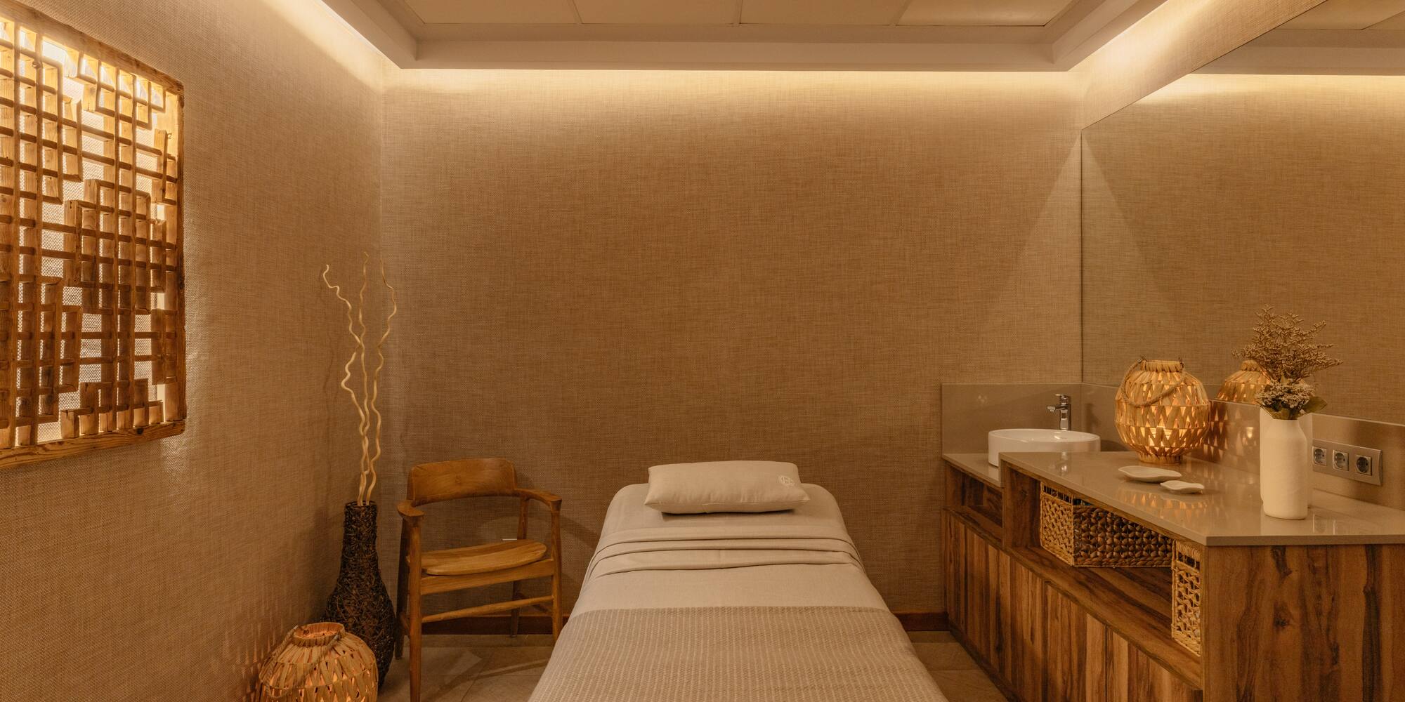 Spa treatment room with massage bed, wooden decor, and warm lighting.