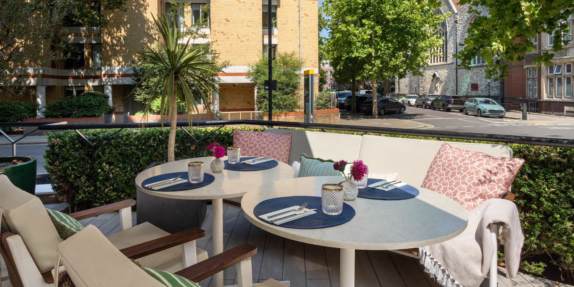 Al fresco dining terrace with set tables, sofa seating, and city street view.