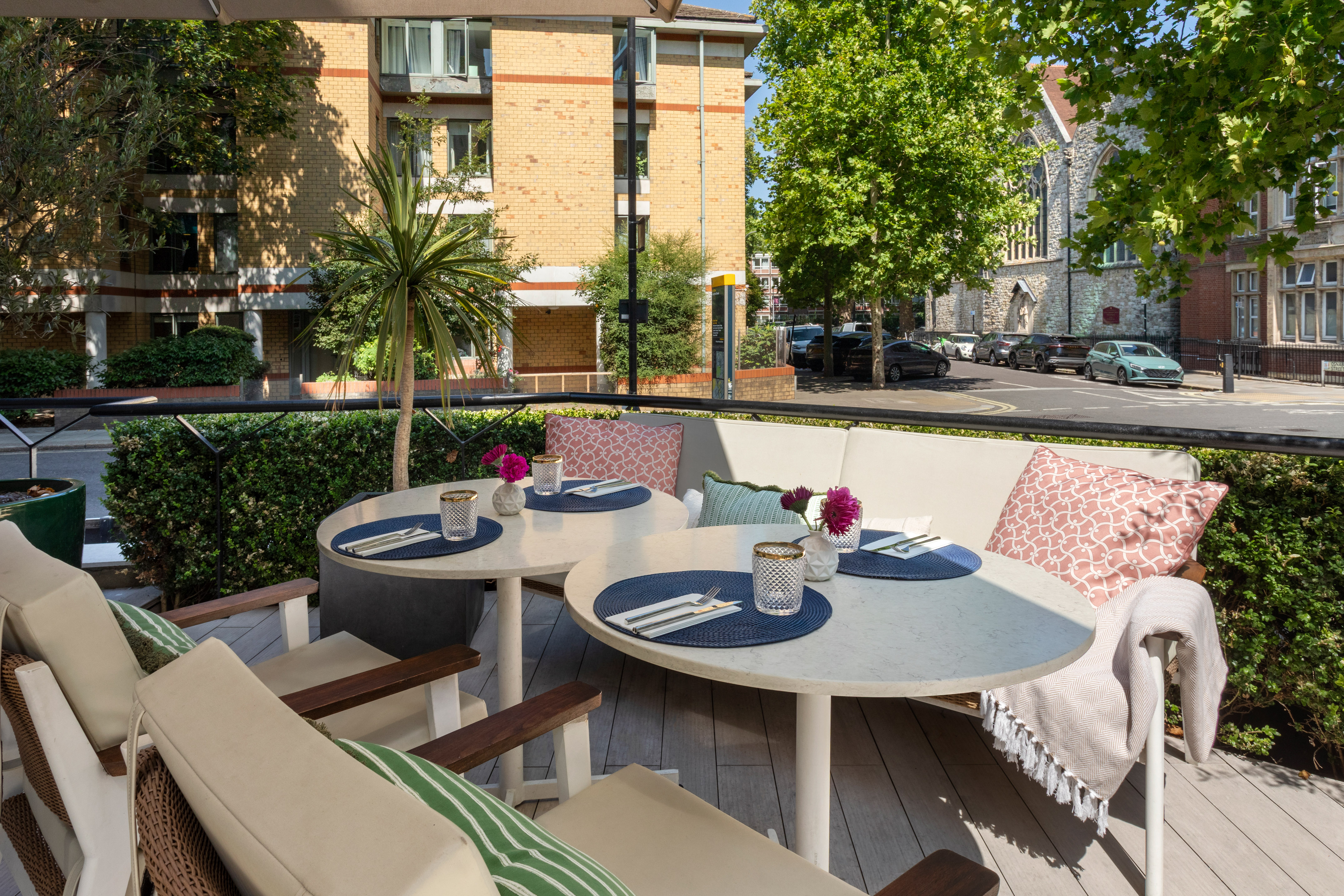 Al fresco dining terrace with set tables, sofa seating, and city street view.
