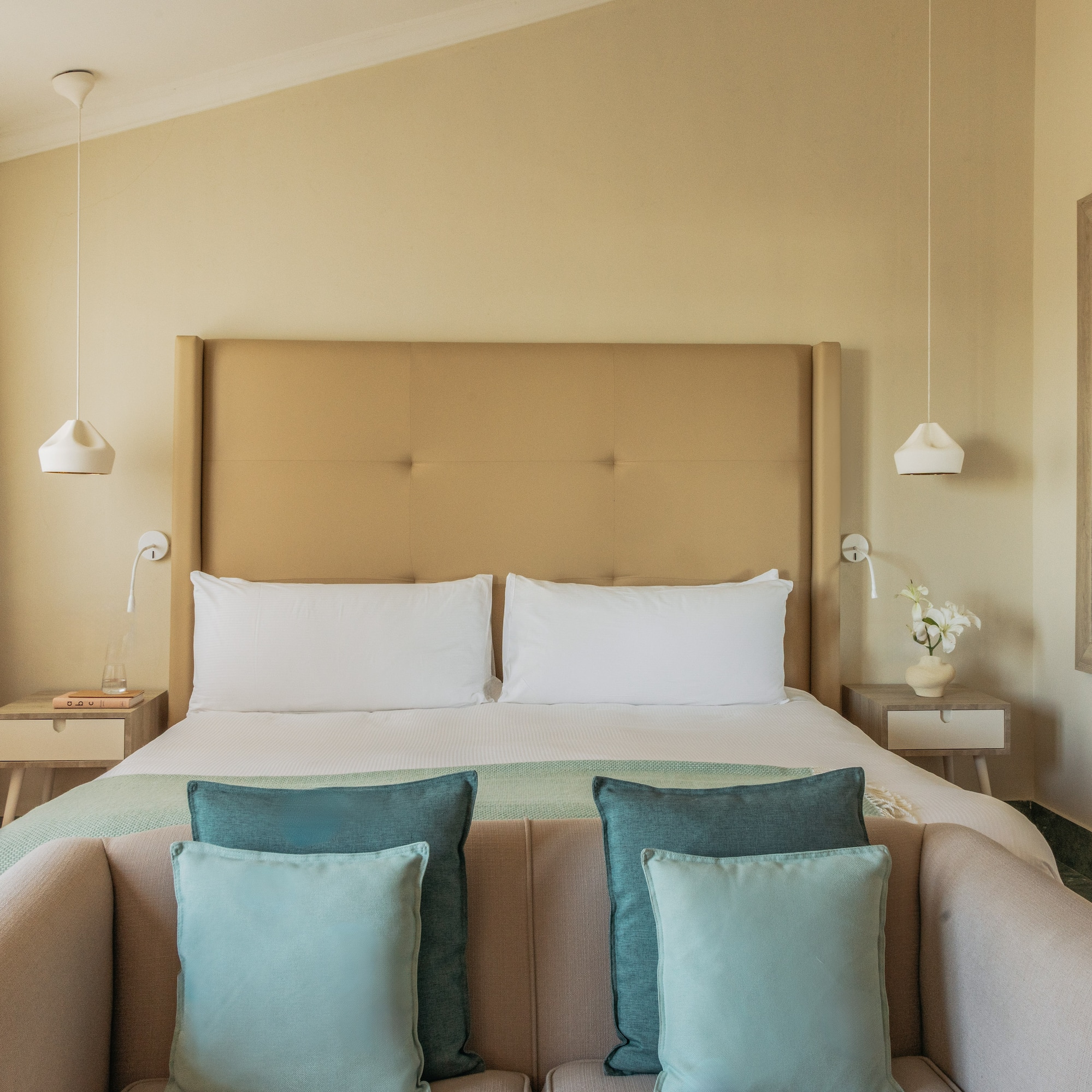 Cozy hotel bedroom with bed, neutral colors, beige headboard, blue accents.