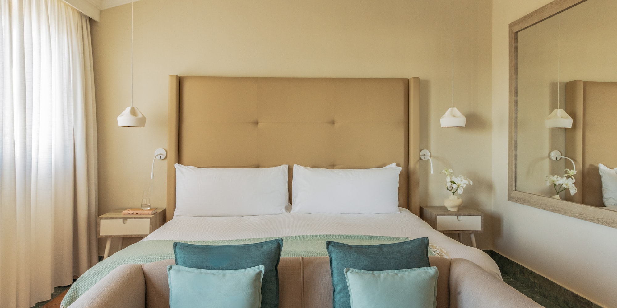 Cozy hotel bedroom with bed, neutral colors, beige headboard, blue accents.