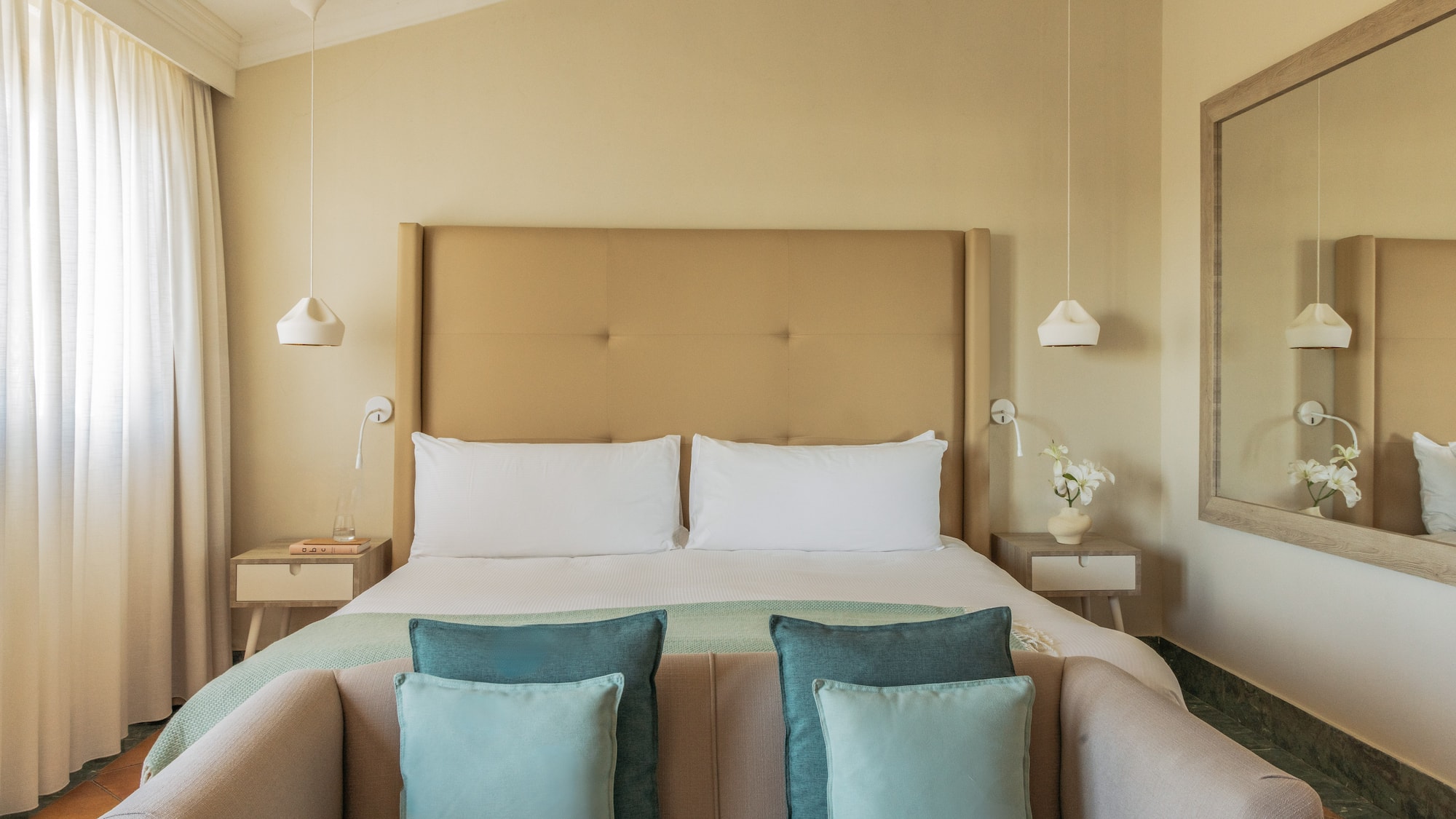 Cozy hotel bedroom with bed, neutral colors, beige headboard, blue accents.