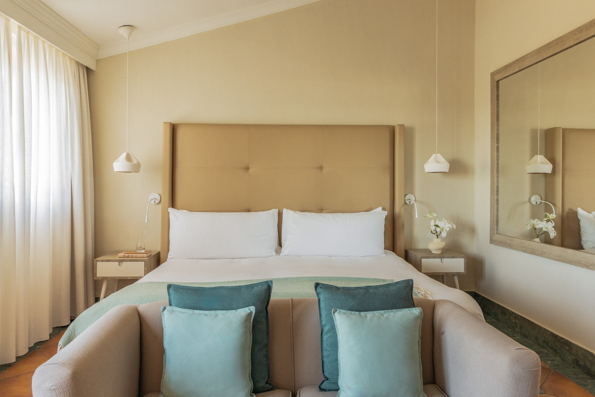 Cozy hotel bedroom with bed, neutral colors, beige headboard, blue accents.