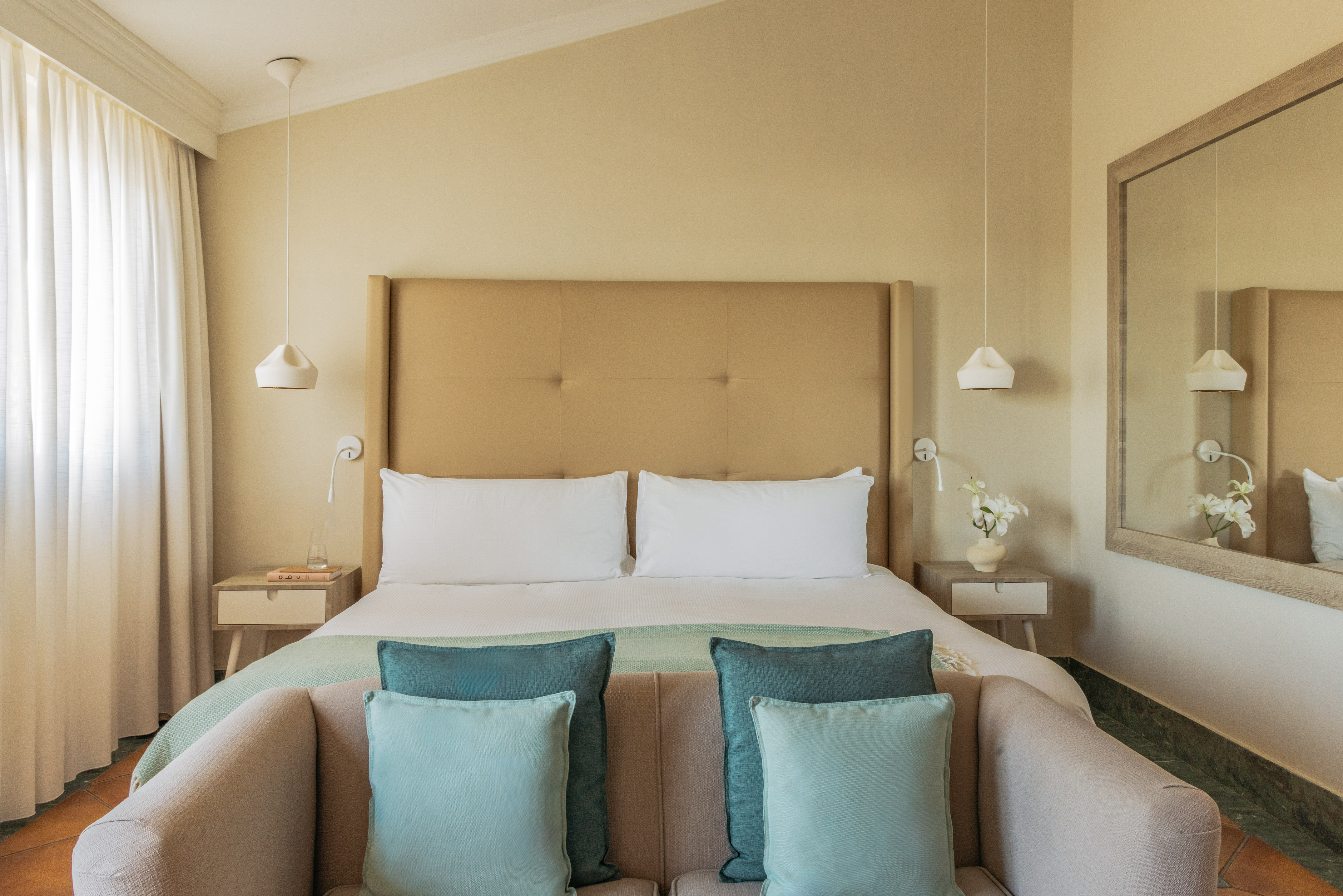 Cozy hotel bedroom with bed, neutral colors, beige headboard, blue accents.
