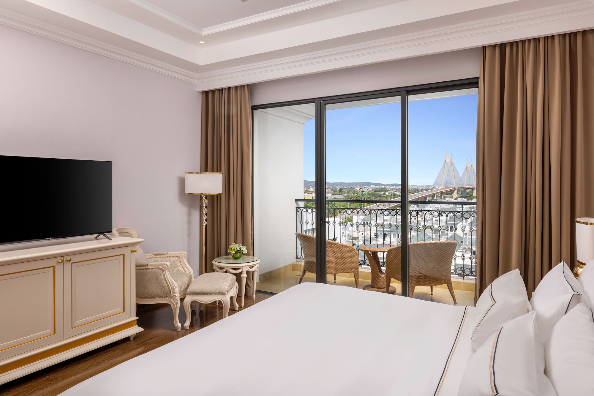 Elegant hotel bedroom with balcony, city view, and suspension bridge.