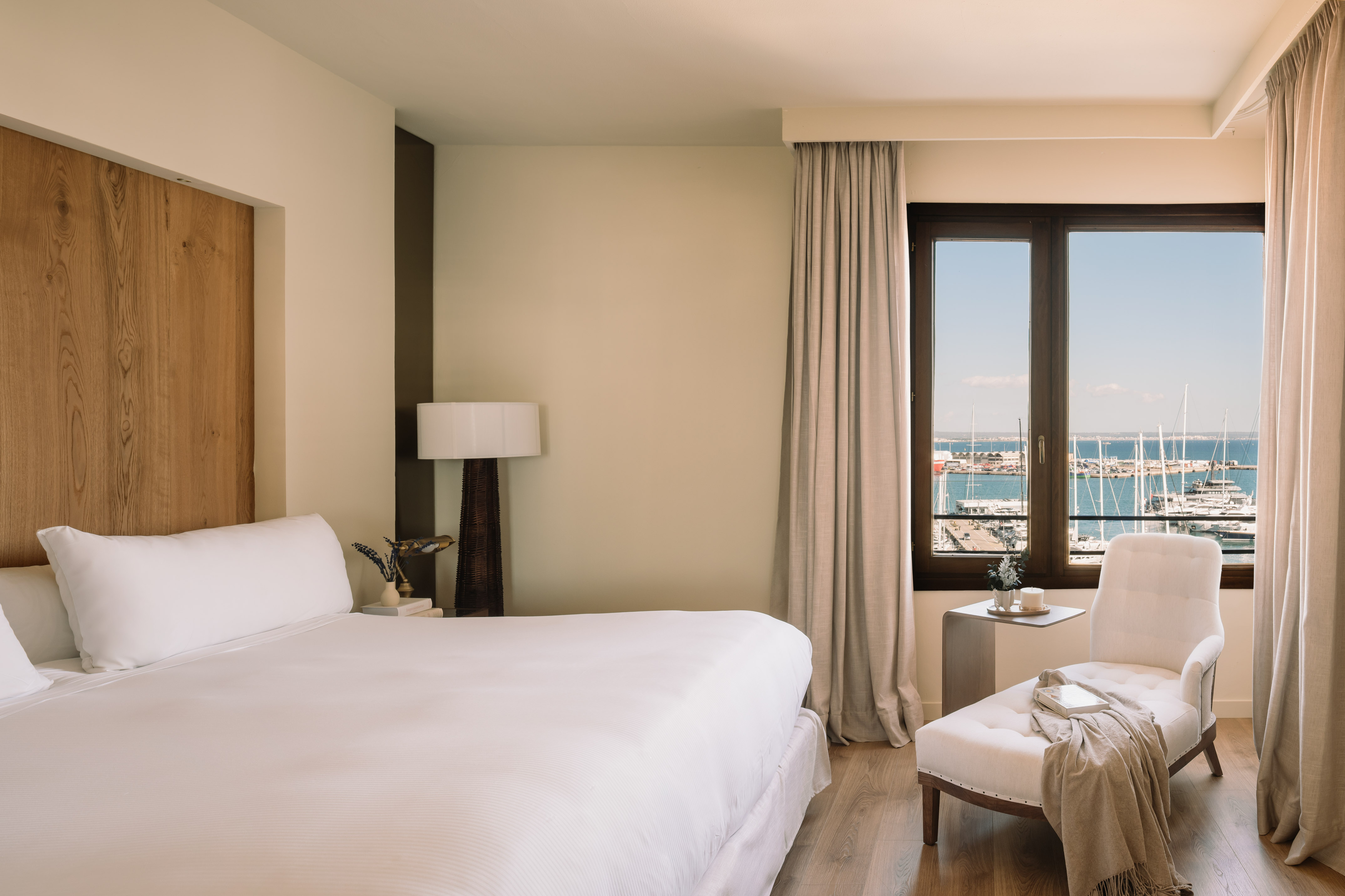 Modern hotel bedroom with large bed, lounge chair, and marina view.