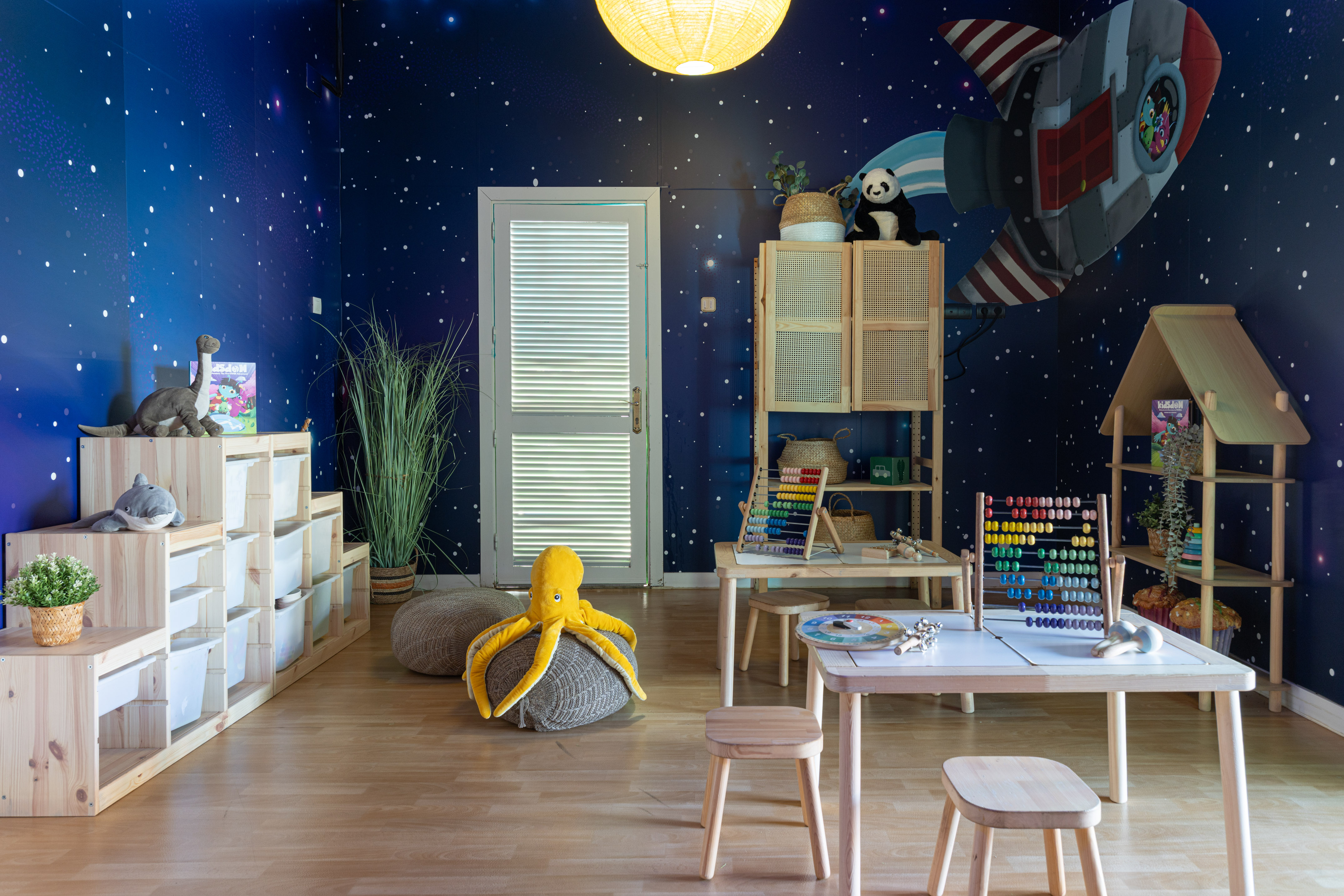 Kids' space-themed playroom with rocket mural, wooden furniture, abacus, and storage.