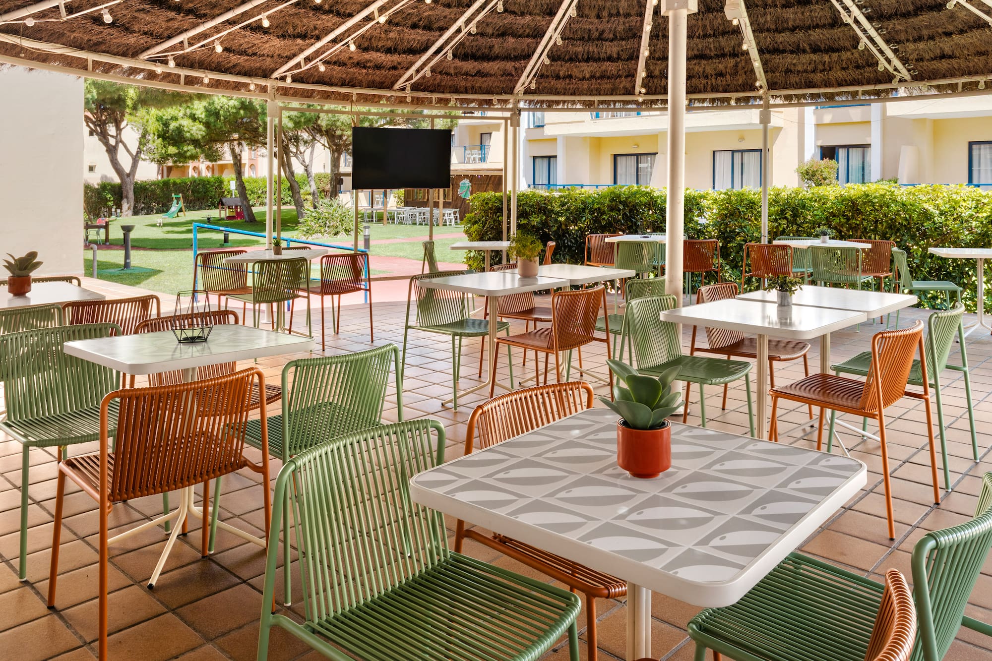 Shaded outdoor patio with green and orange chairs, tables, and garden.