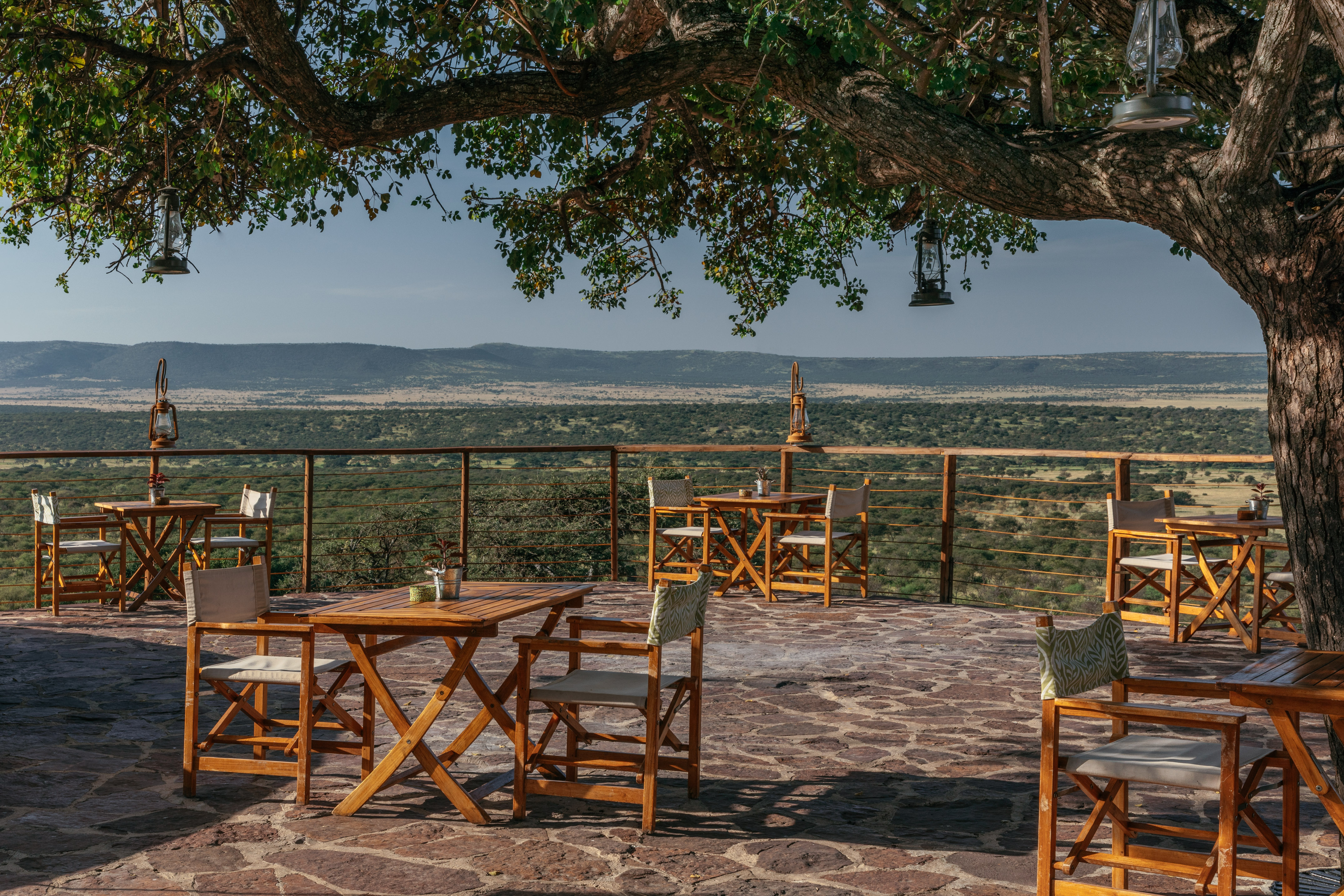 Safari lodge patio with outdoor dining tables, lanterns, and savanna view.