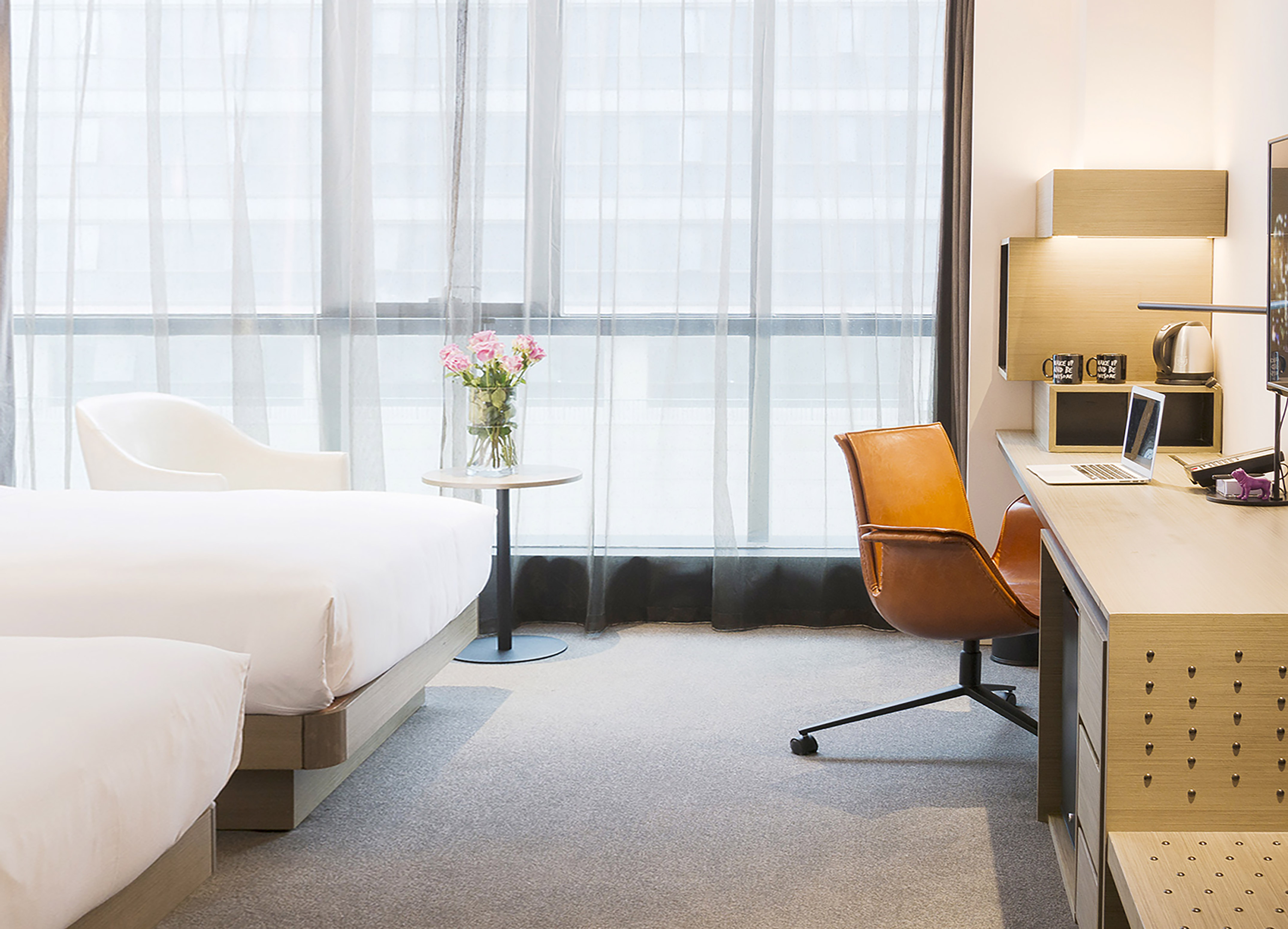 Contemporary hotel room with twin beds, workspace, and large window.