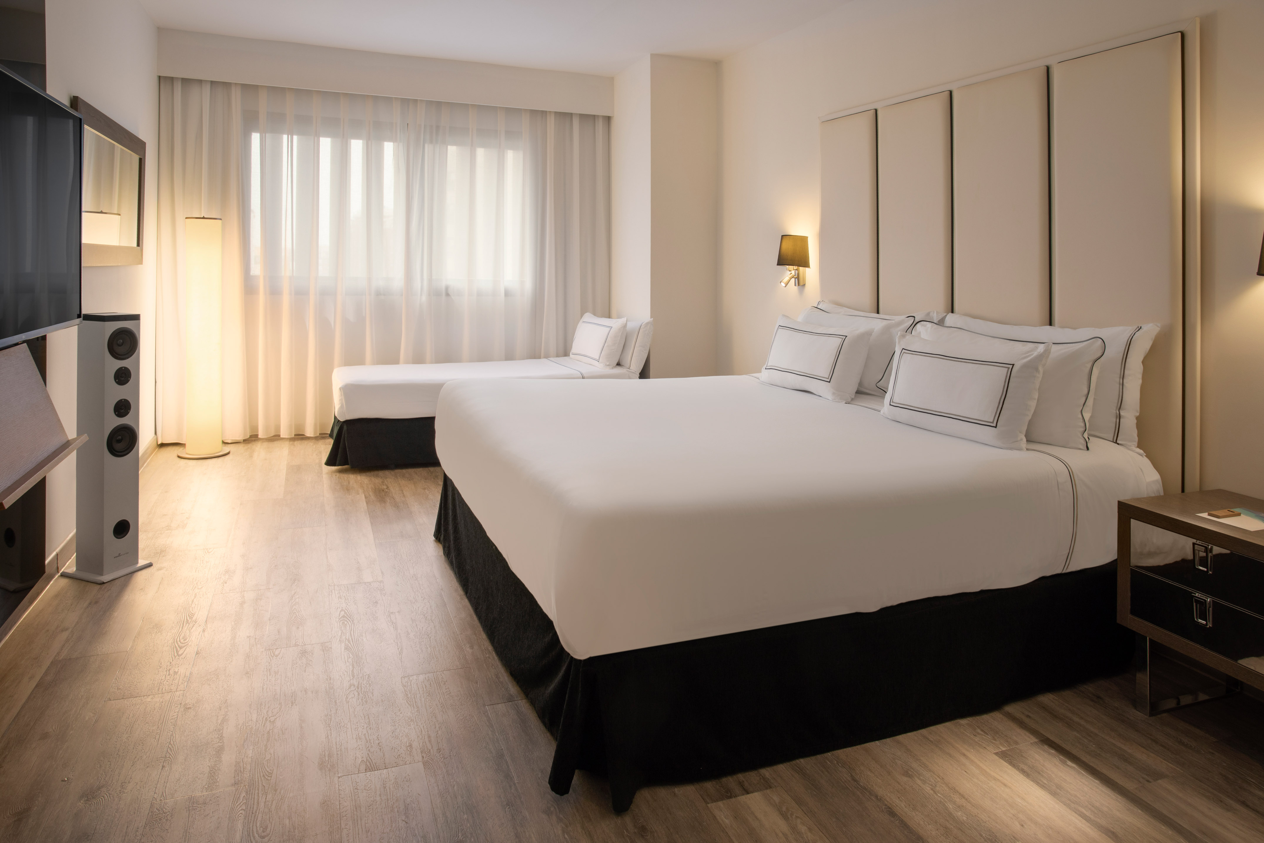 Modern hotel room with double bed, daybed, wood floor, and large window.