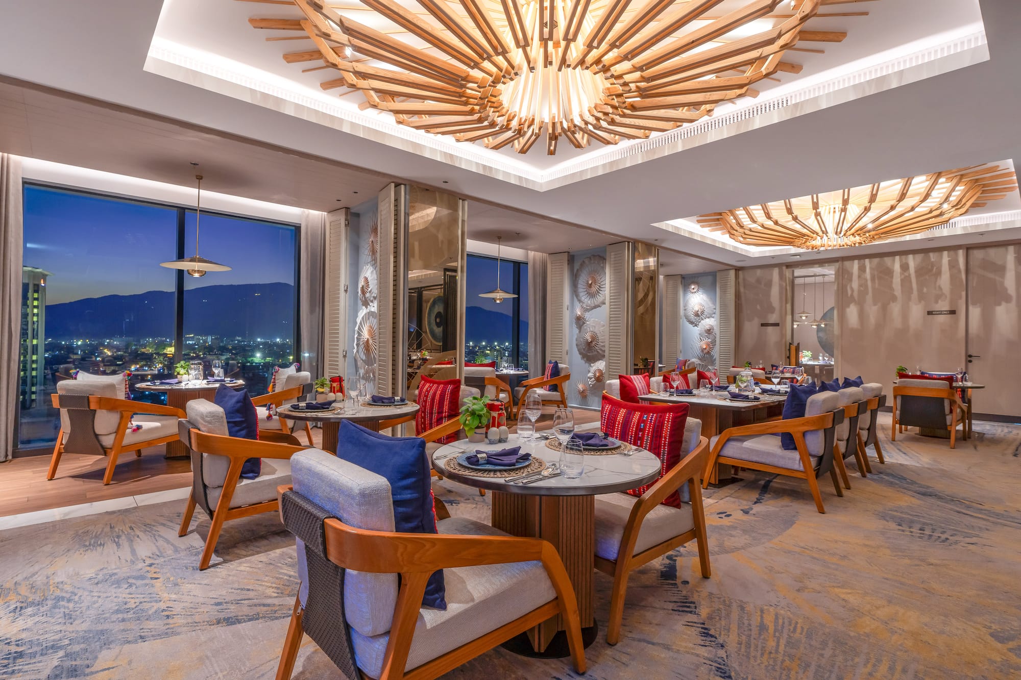 Elegant restaurant with modern decor, wooden chandeliers, and a city night view.