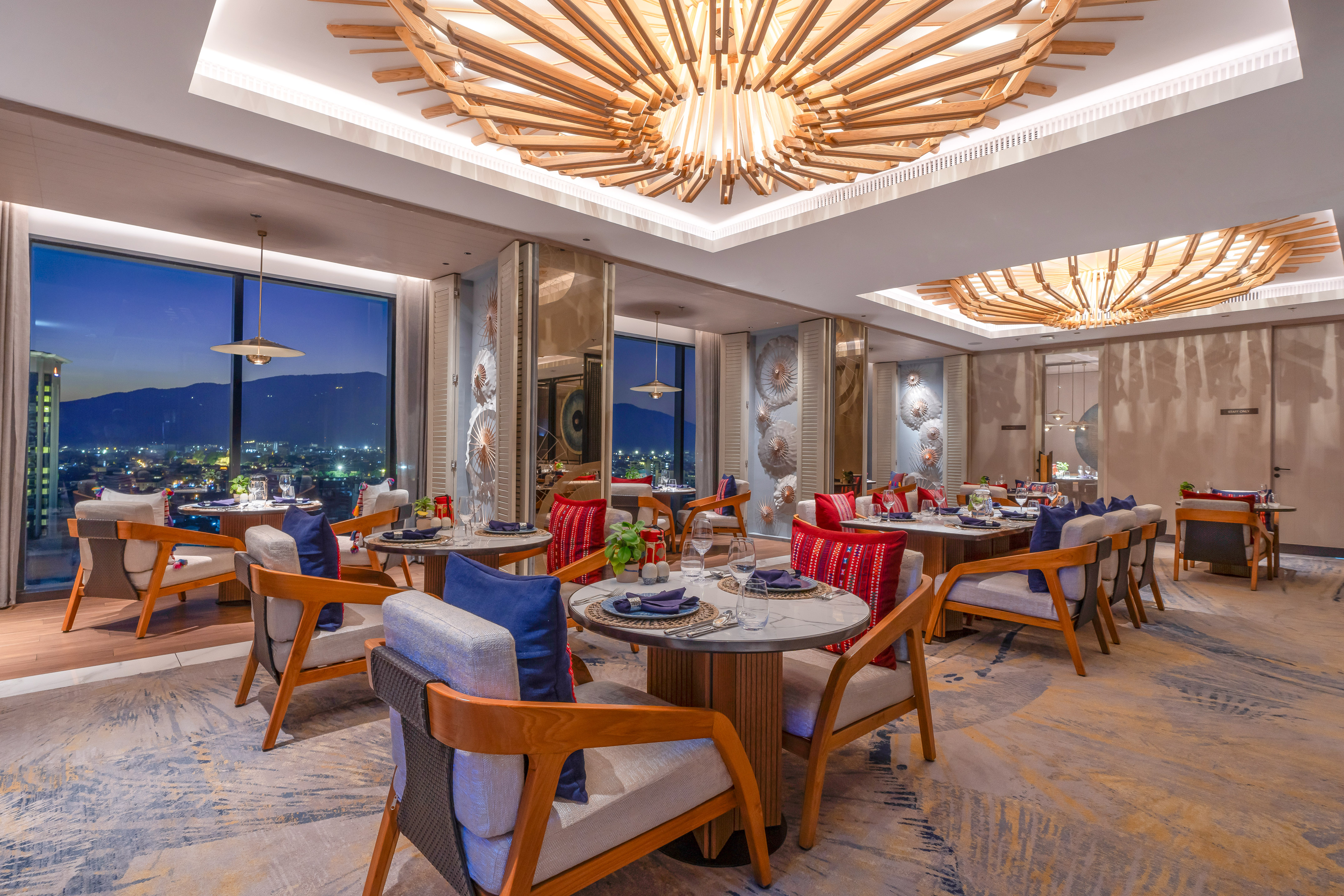 Elegant restaurant with modern decor, wooden chandeliers, and a city night view.