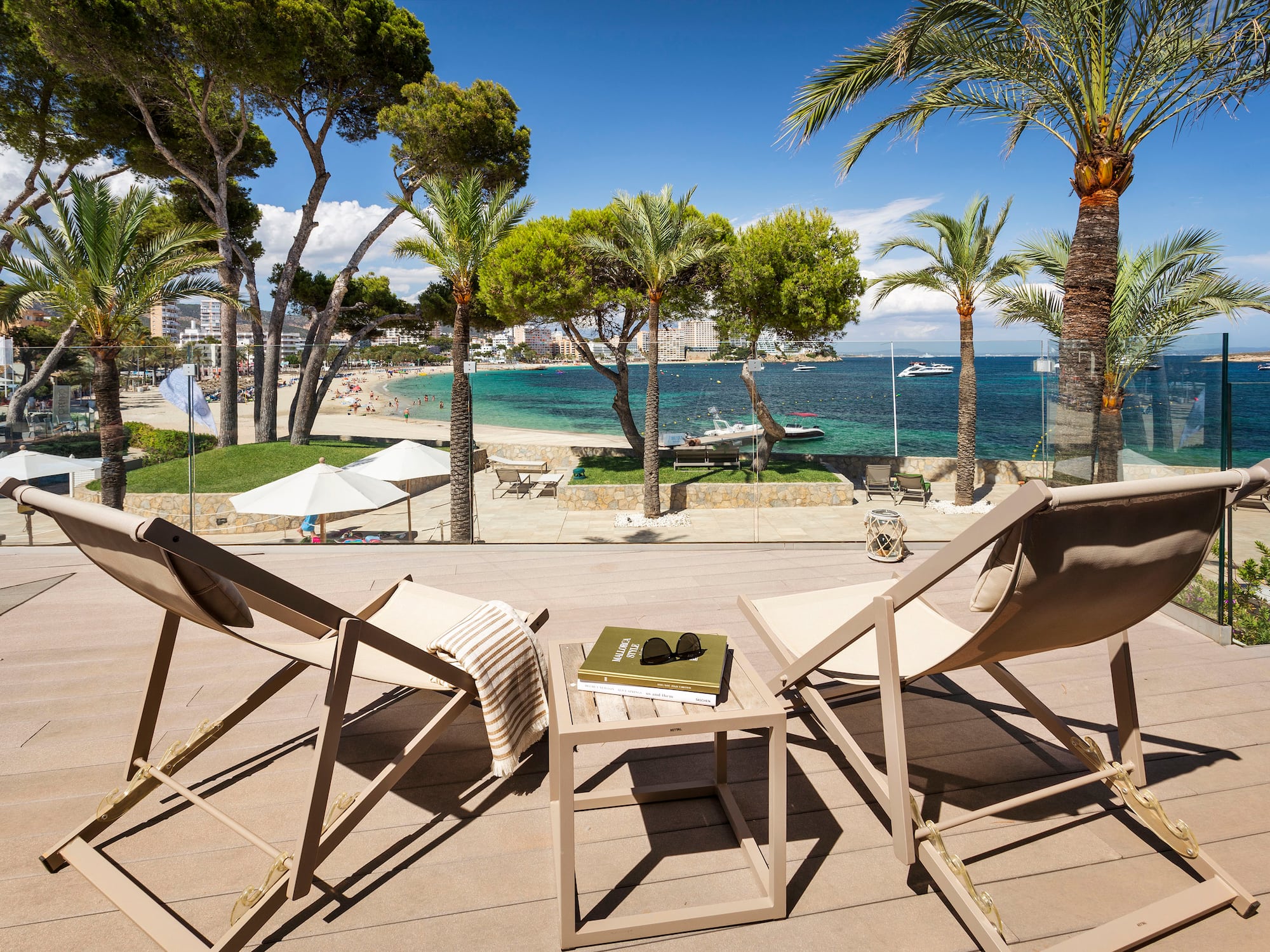 Beachfront patio with lounge chairs, palm trees, and a clear blue sea view.