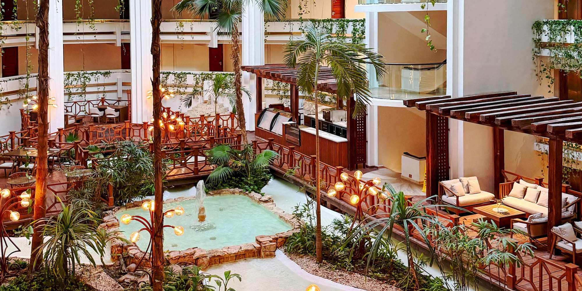 Luxurious resort atrium with indoor garden, winding water, and balcony views.