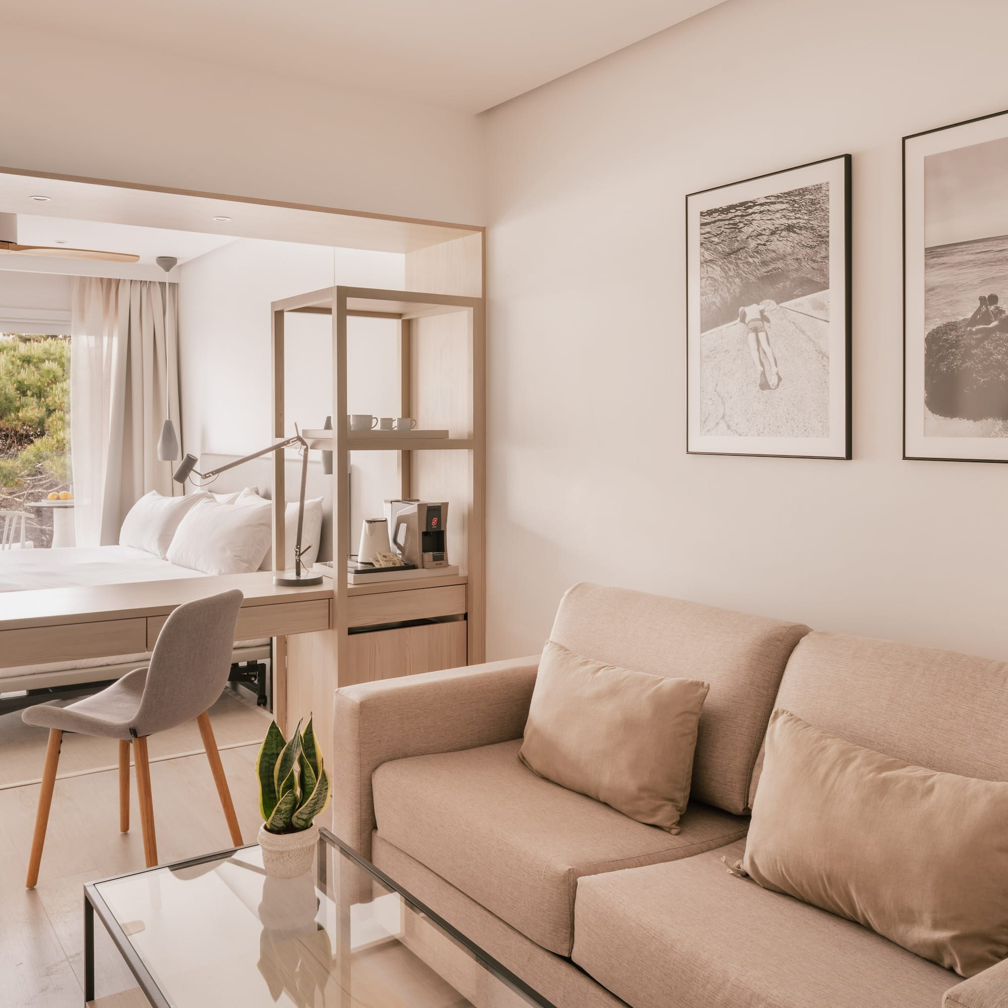 Modern hotel suite with beige sofa, desk, bed, and large window.