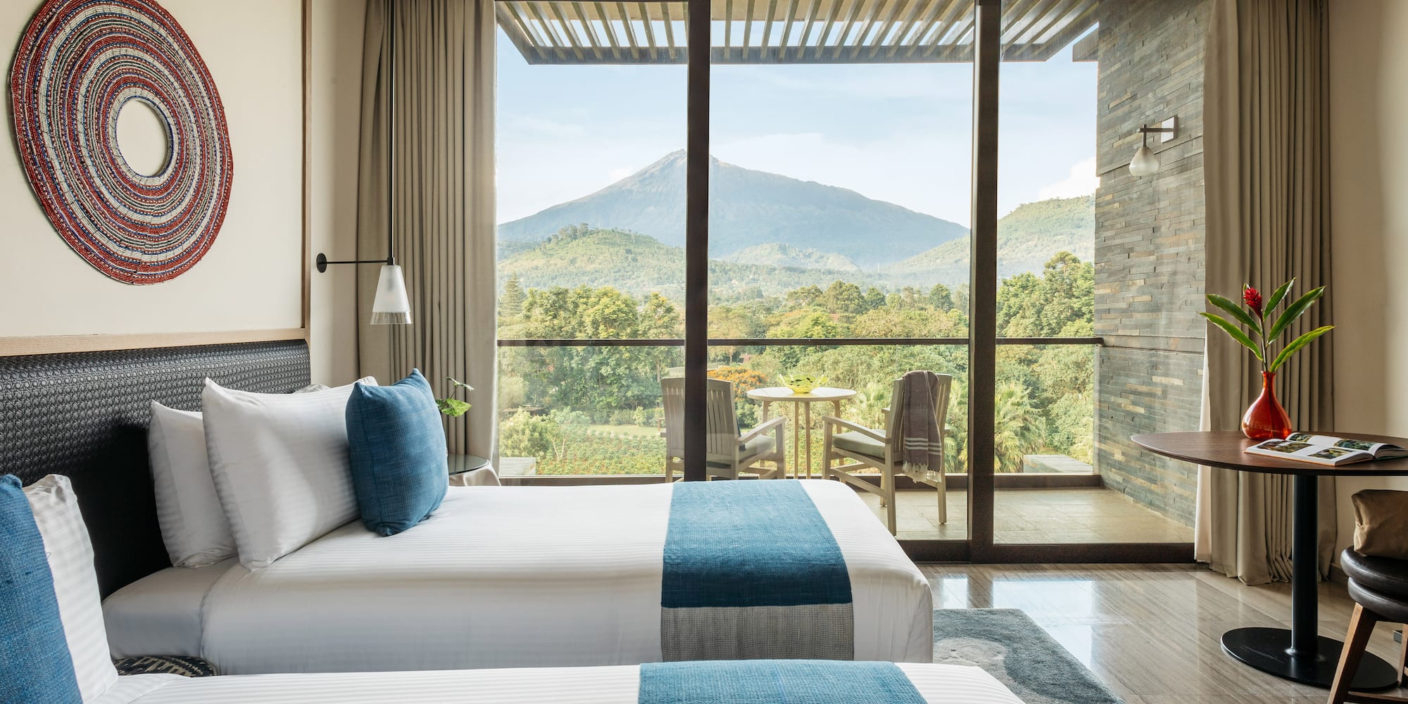 Modern hotel room with twin beds and balcony overlooking lush mountains.