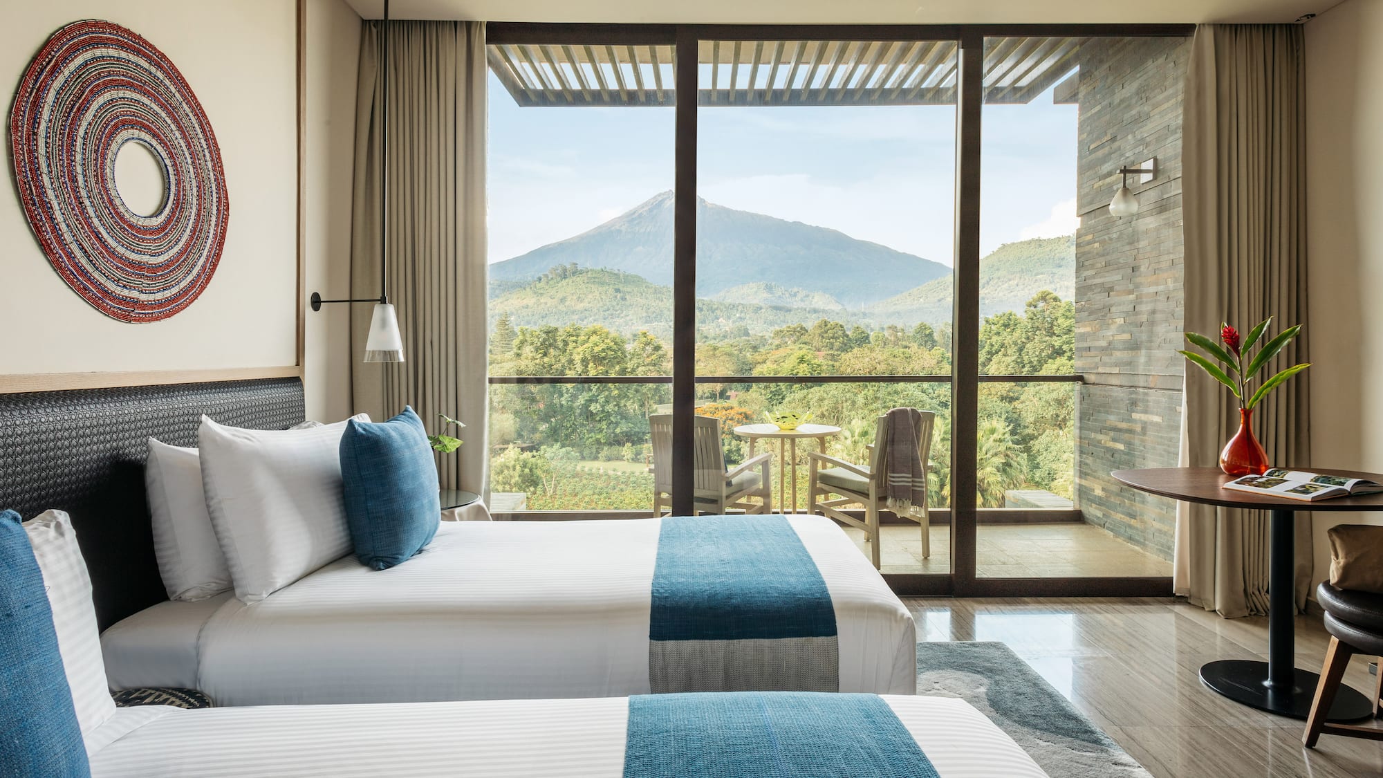 Modern hotel room with twin beds and balcony overlooking lush mountains.