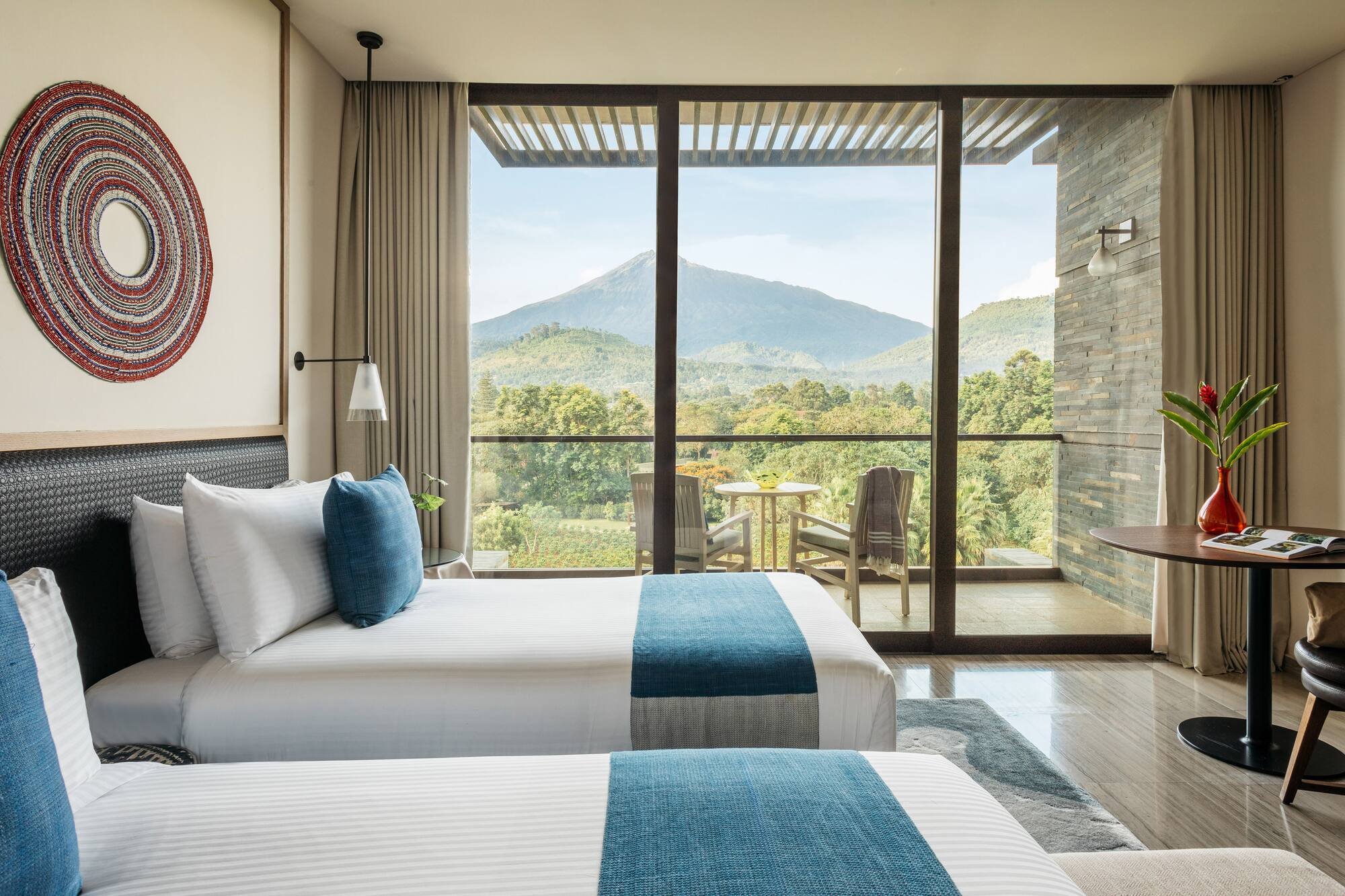 Modern hotel room with twin beds and balcony overlooking lush mountains.