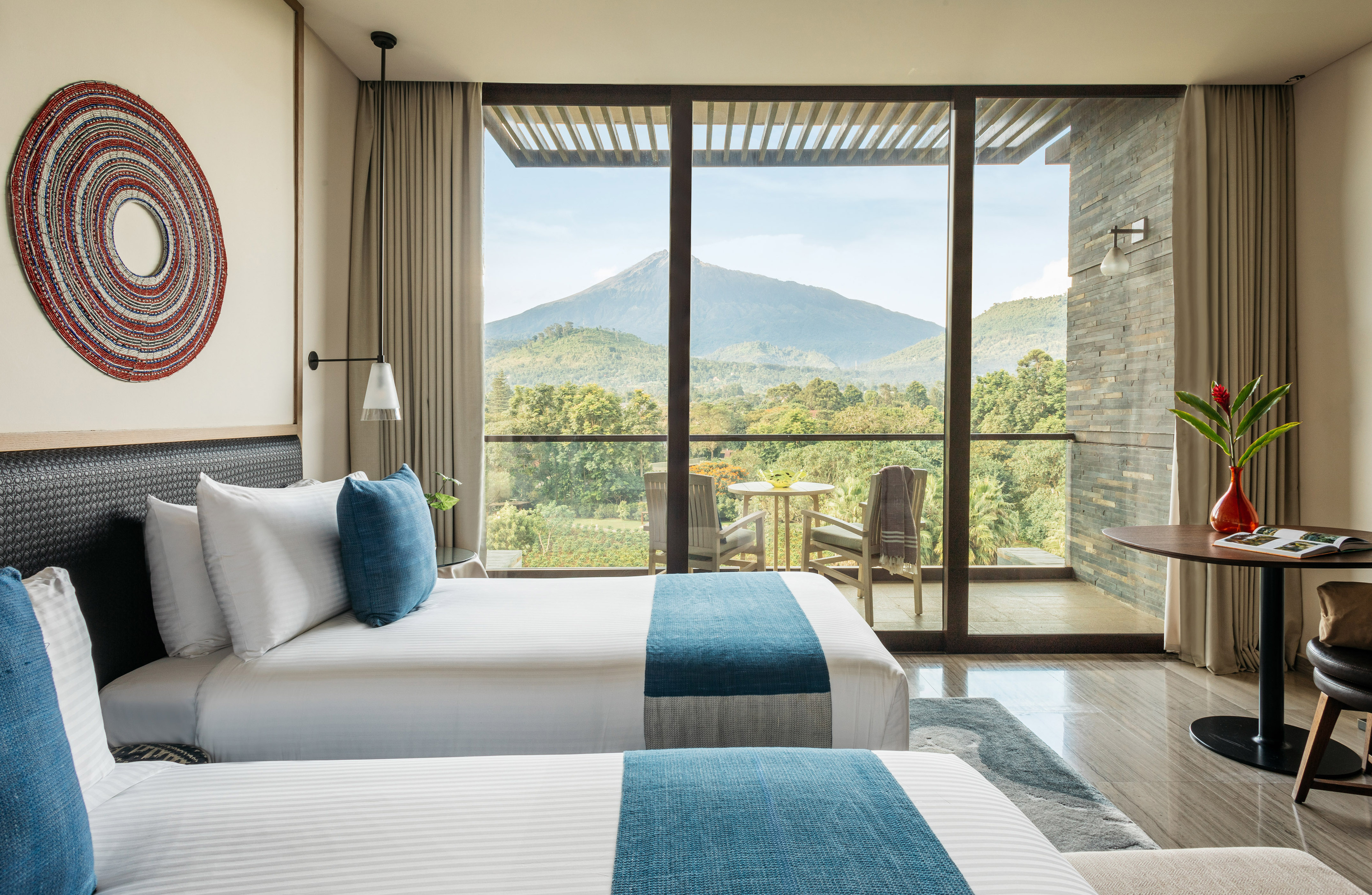 Modern hotel room with twin beds and balcony overlooking lush mountains.
