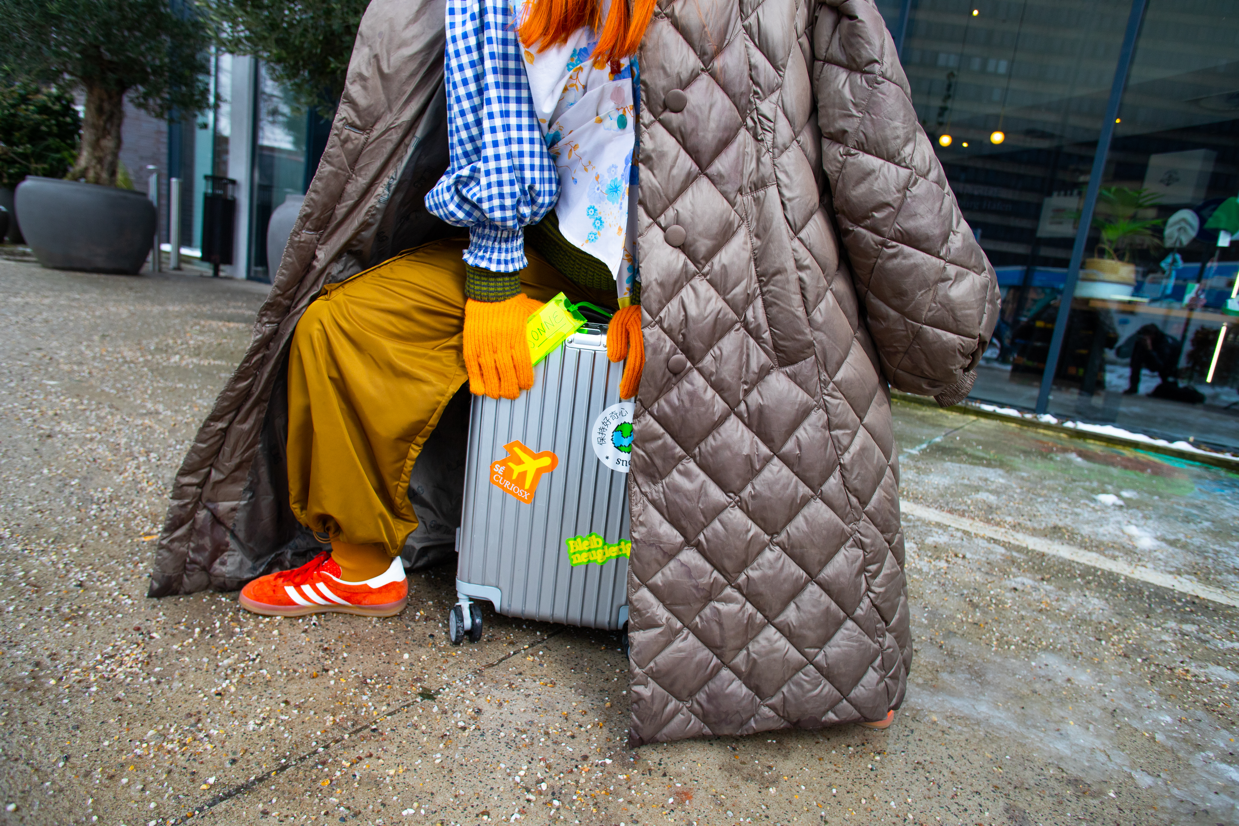 A person wearing a coat and a large overcoat is carrying a suitcase.