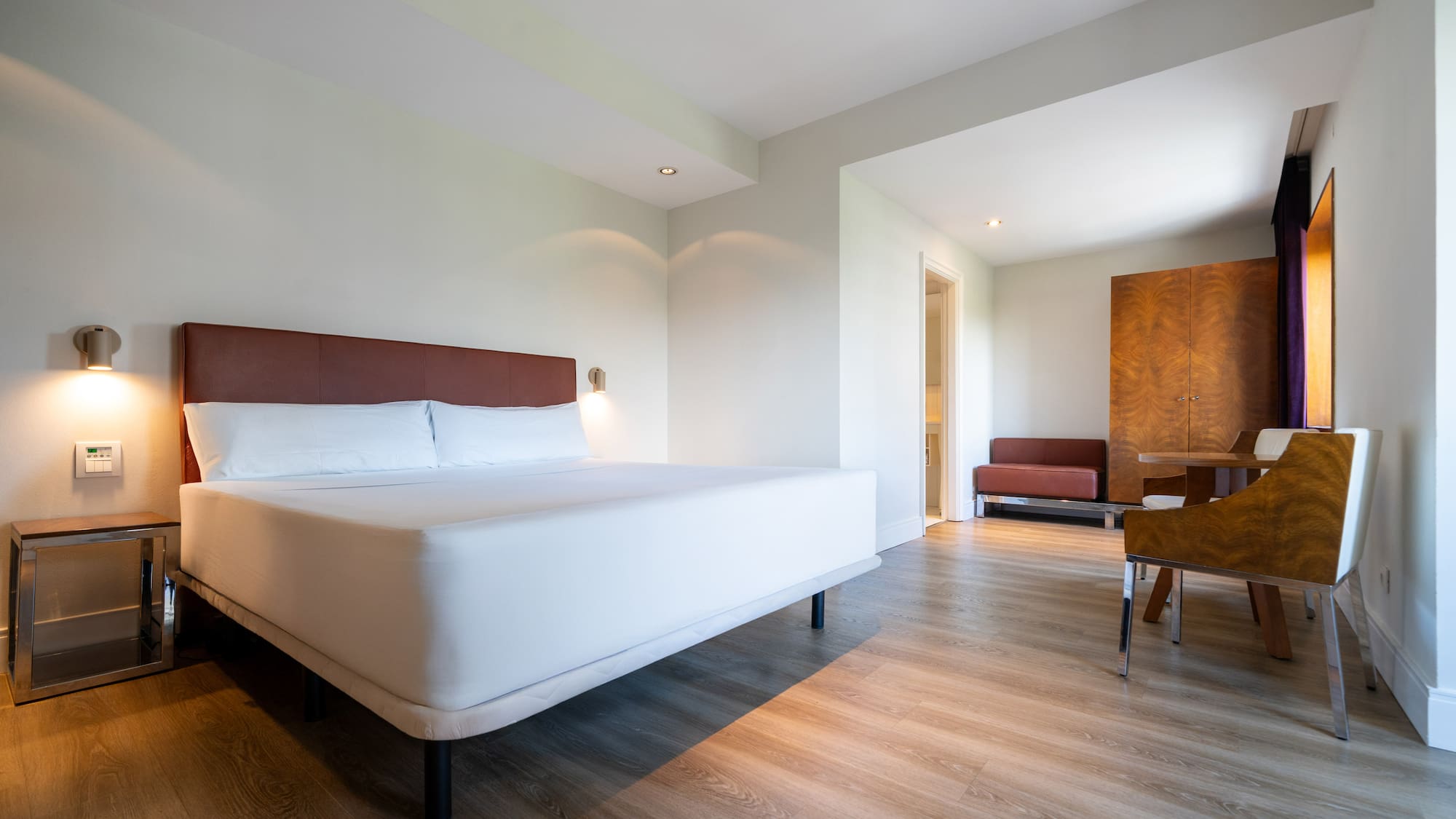Modern hotel suite with white bed, wooden floor, and separate lounge area.