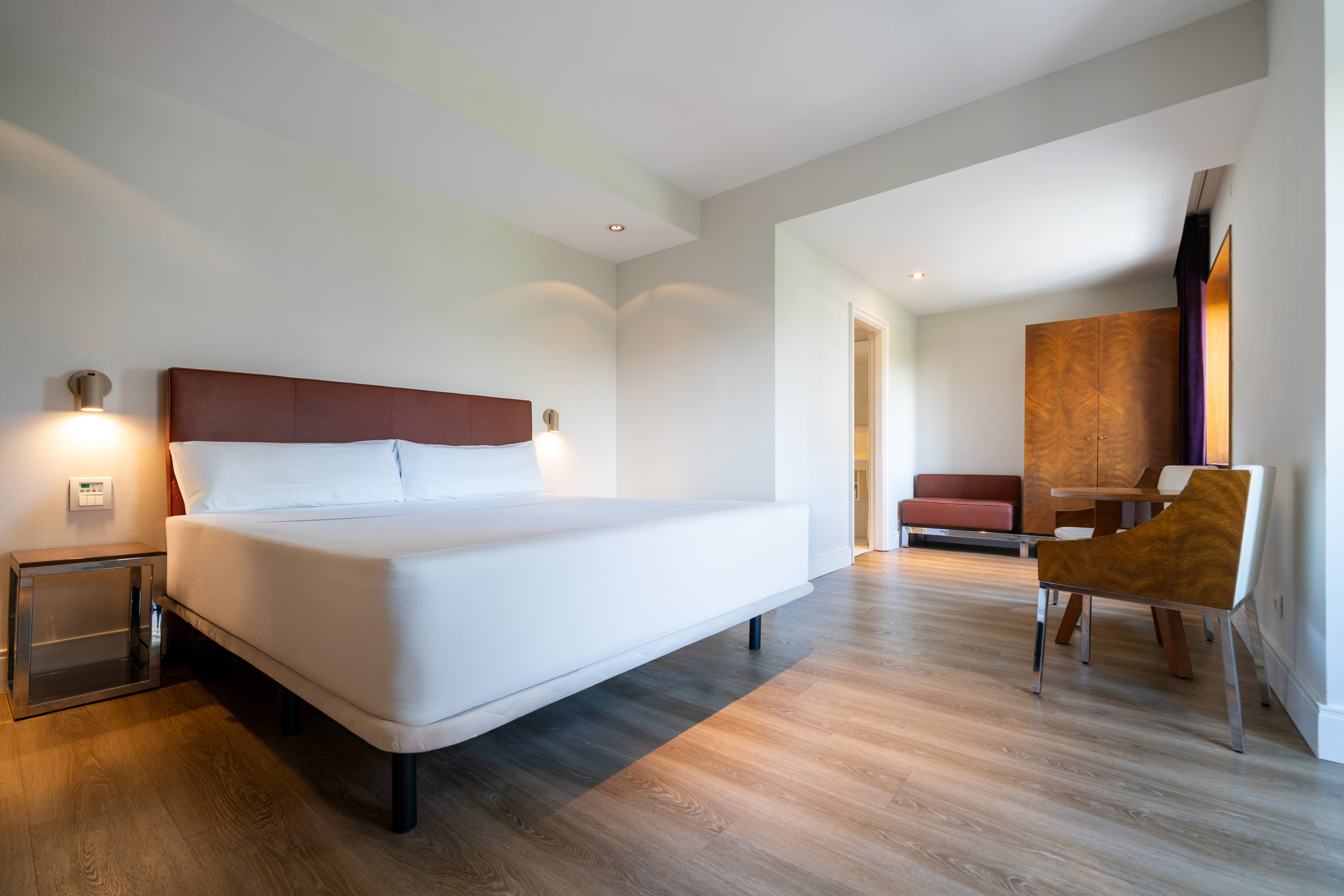 Modern hotel suite with white bed, wooden floor, and separate lounge area.