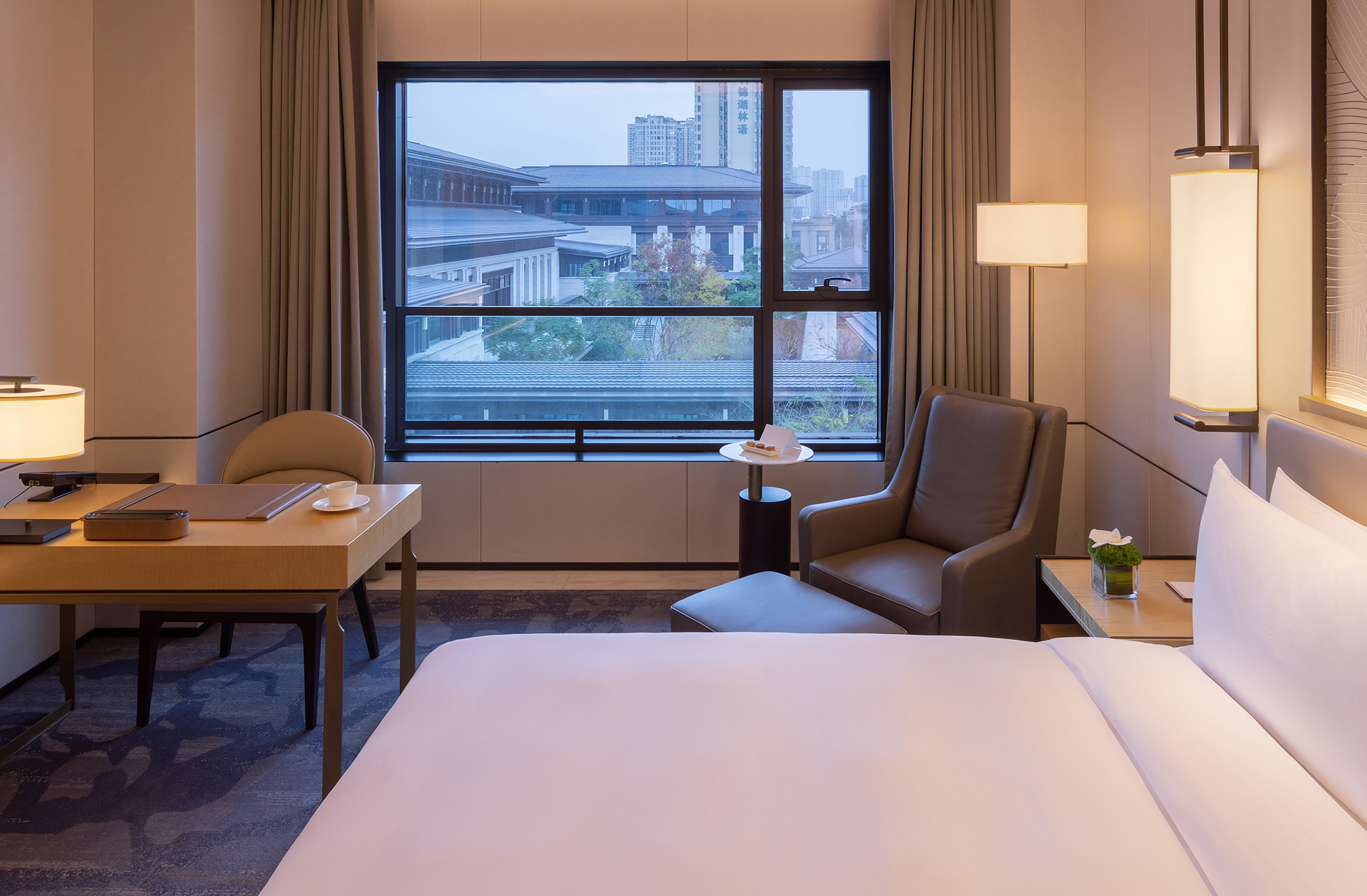 Modern hotel room with work desk, armchair, and large window city view.