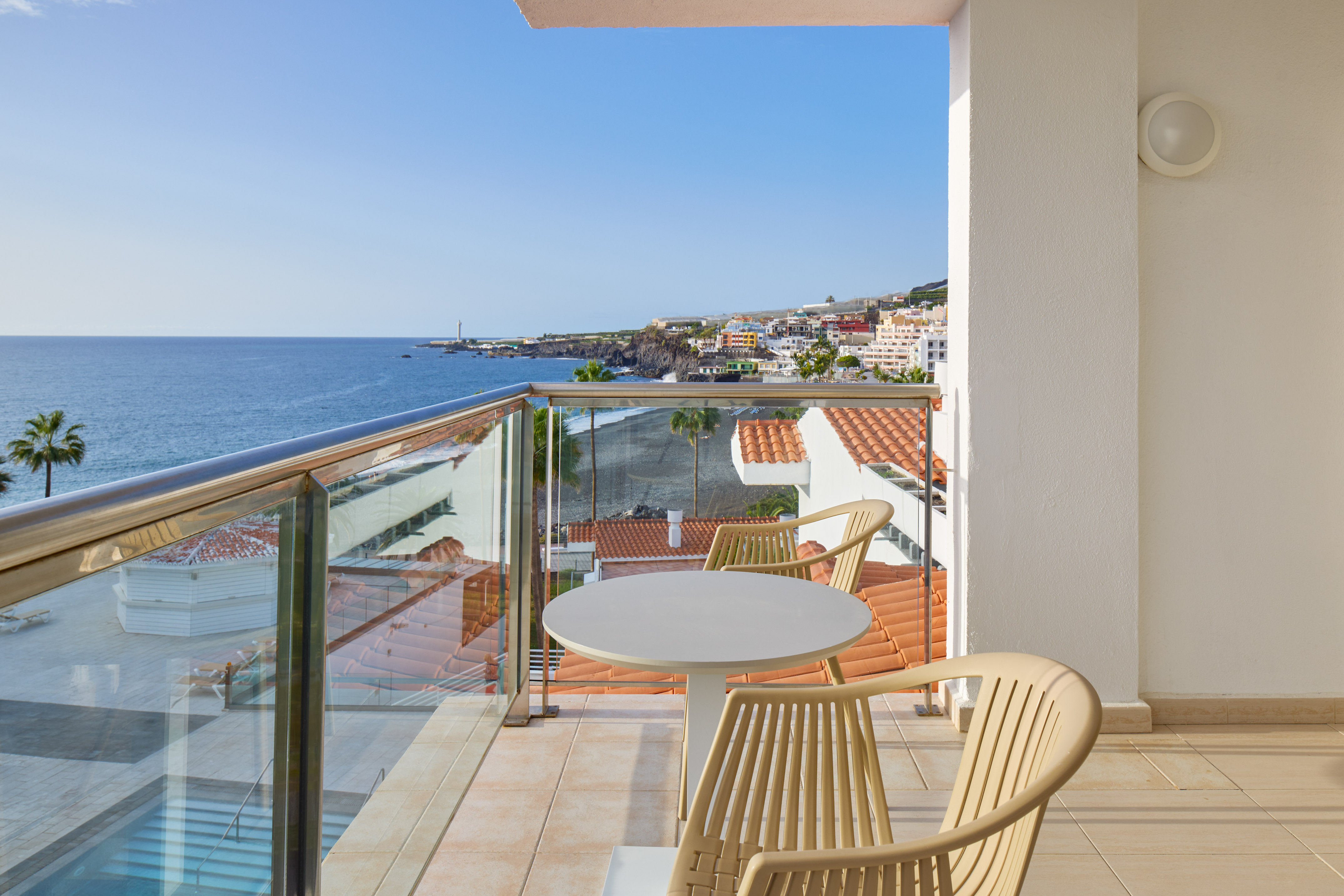 Hotel balcony with sea view, coastal town, and black sand beach.