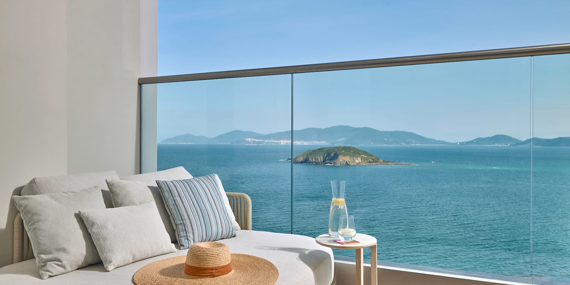 Balcony daybed with ocean island view, straw hat, and refreshing drink.
