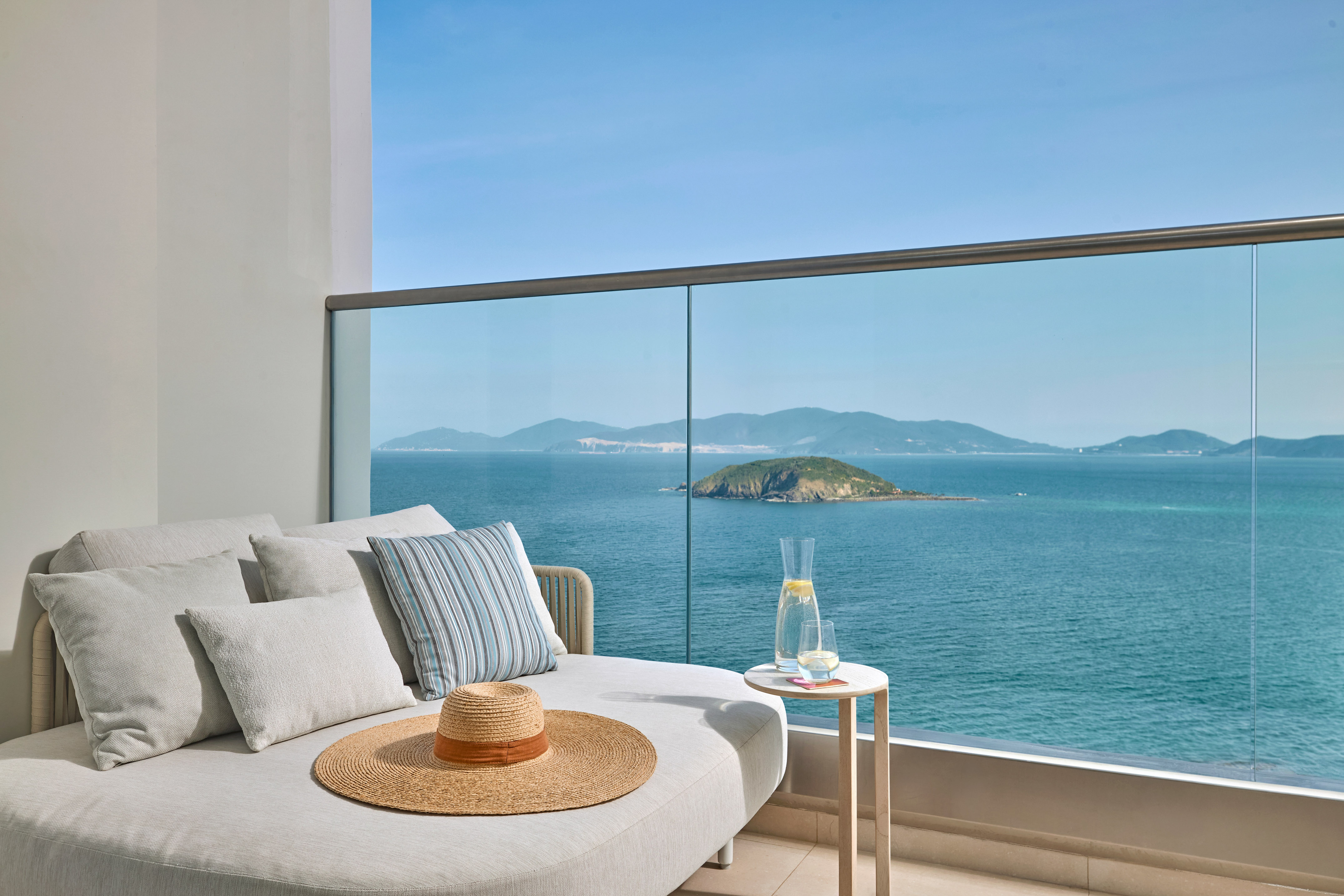Balcony daybed with ocean island view, straw hat, and refreshing drink.