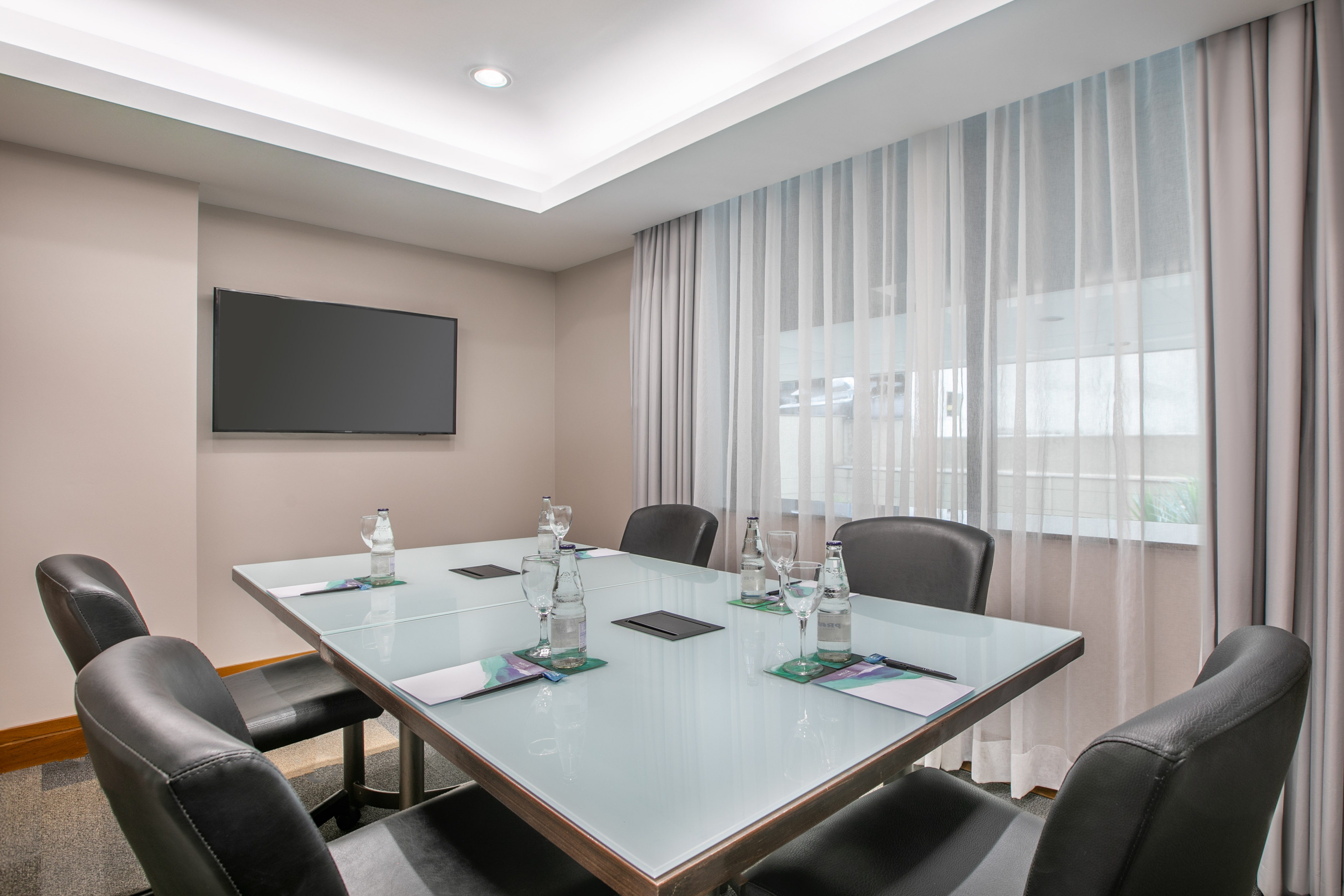 Modern corporate meeting room with glass conference table, chairs, TV.