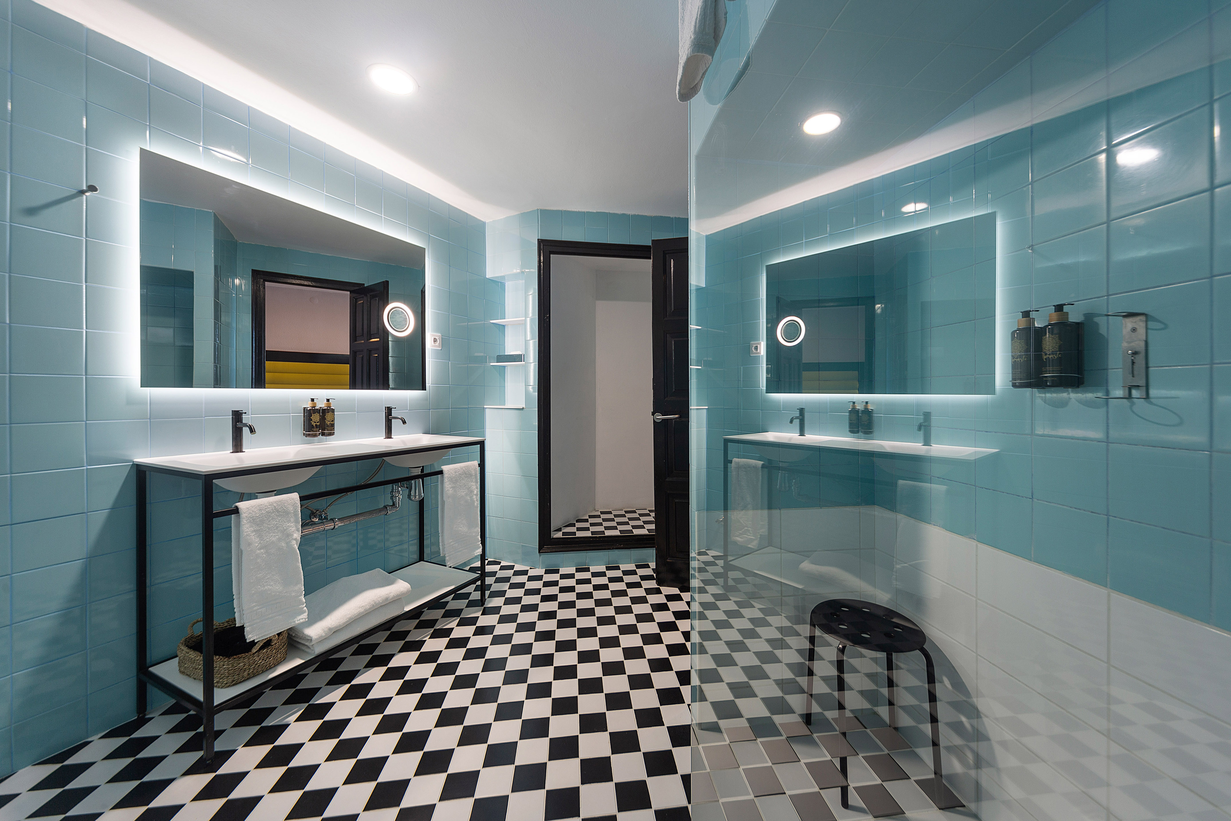 Modern blue tile bathroom with double vanity, lighted mirrors, and checkered floor.